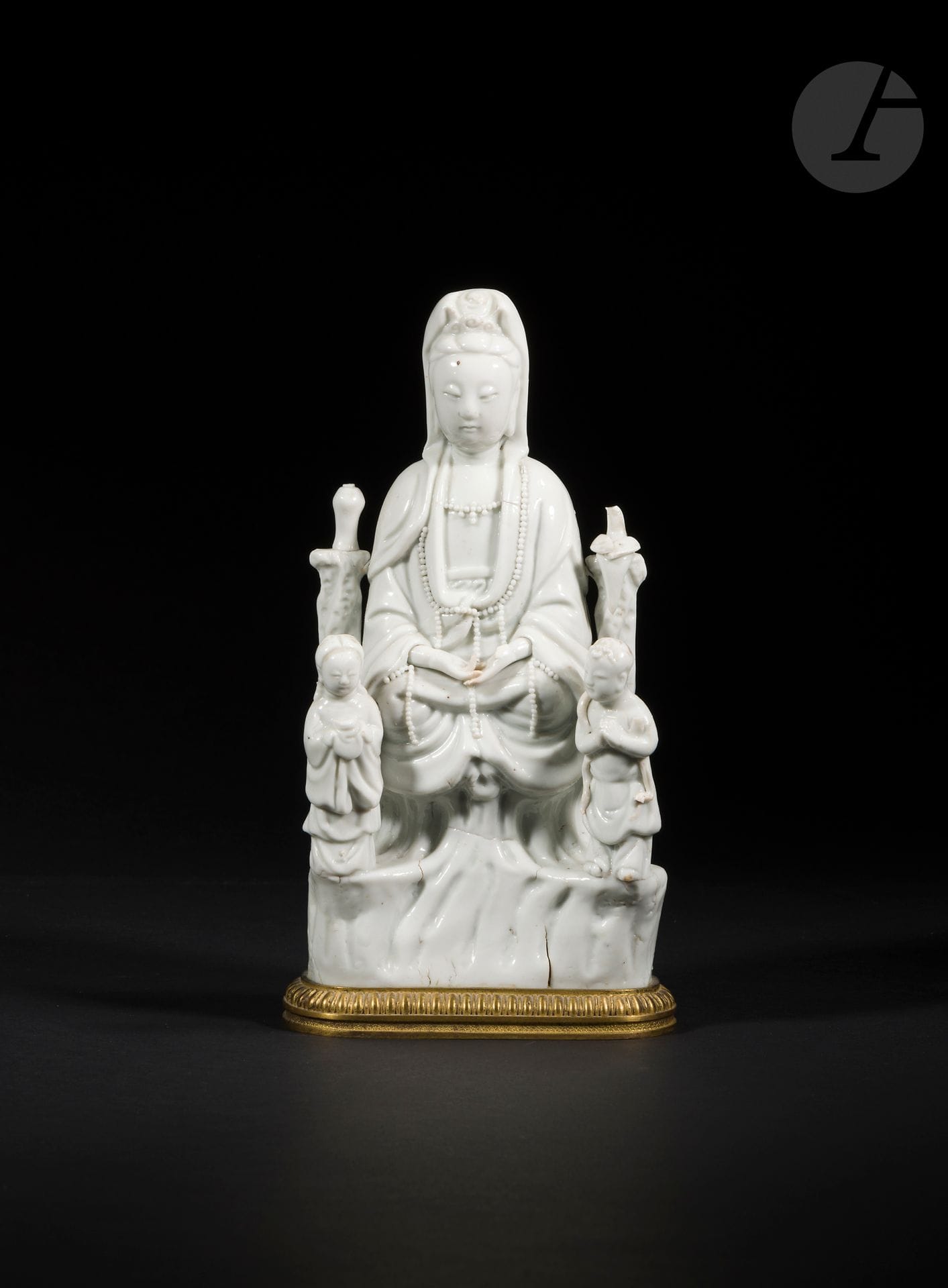 Guanyin in Chinese white porcelain, China, Dehua, 17th century
Depicted seated in dhyanasana on a rock, she is dressed in a pleated robe open to the chest and adorned with a long pearl necklace. She is surrounded by two stone columns on which rests a vase and a parrot. Standing at her feet are LongNü, holding the Pearl of Light, and ShanCai TonZi, hands in adoration.
Height: 22 cm
Mounted on a gilded copper alloy base. Missing thumbs and bird's head.