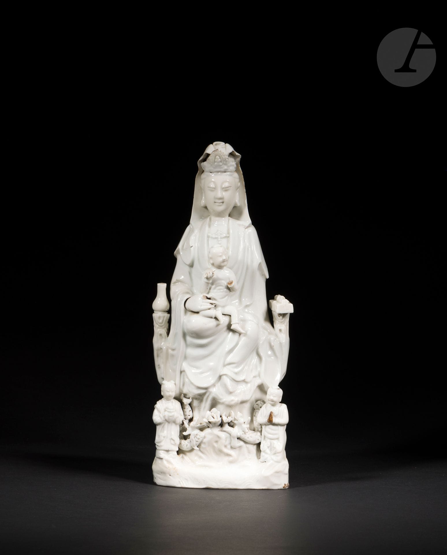Large Chinese white porcelain Guanyin, China, Dehua, 18th century
Depicted seated with her right leg bent, her left leg dangling in a position known as vāmārdhaparyaṅka, and holding a seated child. A lustral water flask to her right placed on one side of her throne, a scroll and sutra books to her left. At his feet, his two acolytes LongNü, holding the Pearl of Light and ShanCai TonZi, hands in adoration. Between them, on a terrace, a lotus flower surrounded by two facing dragons.
Height: 37 cm
Minor accidents.
