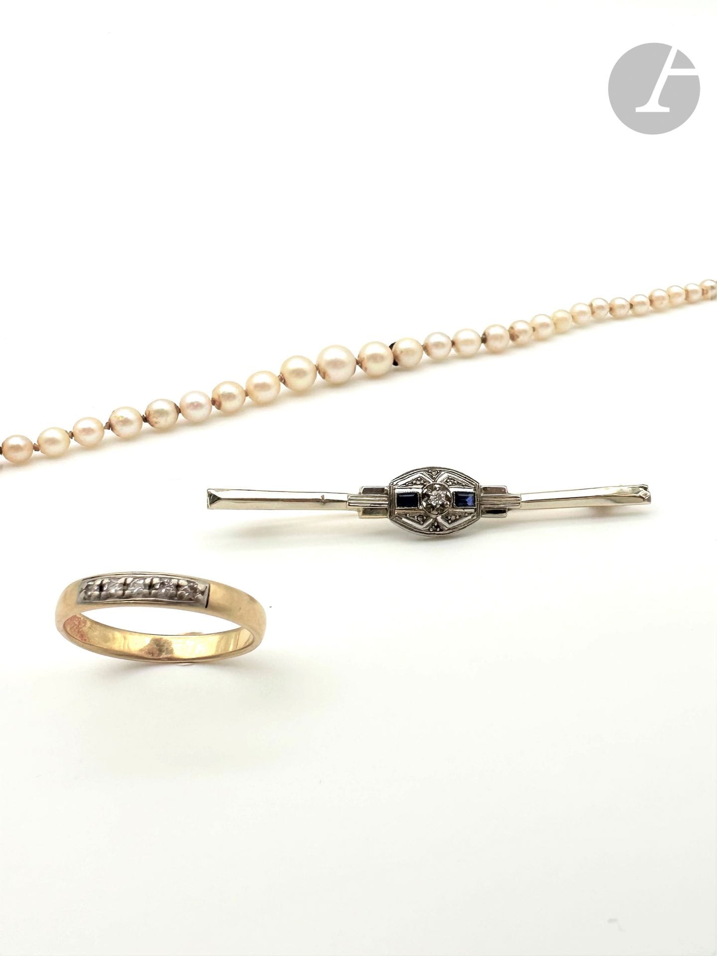 Jewelry lot in 18K (750) gold comprising: a ring set with 5 round brilliant-cut diamonds; a necklace of tumbling cultured pearls, the clasp in 18K gold; and a line brooch adorned with a platinum motif pierced with geometric motifs and studded with rose-cut diamonds, set with an 8/8 round diamond backed by rectangular sapphires. Finger size: 58. Necklace length: approx. 47 cm. Brooch length: approx. 6 cm. Gross weight: 17.9 g (shocks, chips, dents, deformations).
