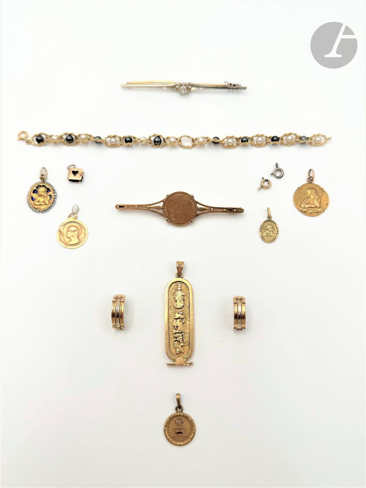 Lot de bijoux en or 18K (750) comprenant : un bracelet agrémenté de perles de culture ; une broche fuseau sertie d'un diamant rond de taille ancienne ; une broche ornée d'une pièce de 10 francs or ; cinq médailles ; un pendentif-cartouche égyptien et une paire de demi-créoles en deux tons d'or 14K (585). Poids brut : 52 g (usures, déformations, manque)