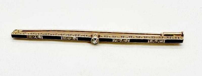 Broche-barrette en or 18K (750) et platine, sertie d'une ligne d'onyx calibrés scandée de diamants taillés en rose et centrée d'un diamant rond de taille ancienne. Travail des années 1920. Longueur : 7,2 cm environ. Poids brut : 4,9 g (choc, égrisures)