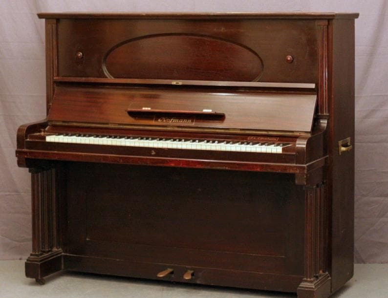 Piano droit Hofmann en acajou foncé Cadre métallique Cordes croisées Sommier découvert. Clavier ivoire de sept octaves Equipé d'une molliphone (sourdine) Fait à Vienne, 1925 Hauteur 134 cm x Largeur 154 cm Partie harmonique intacte, instrument en bon état. Piano de qualité, puissant et rond
