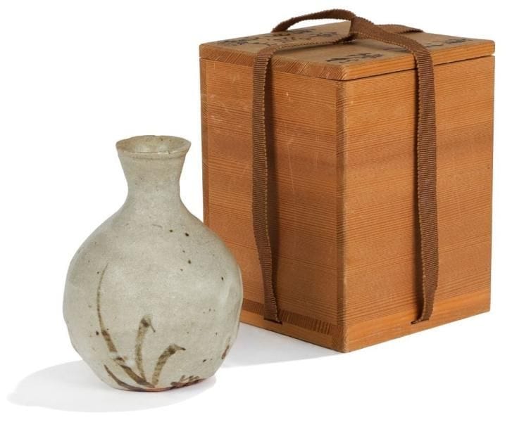 Arakawa TOYOZO (1894-1985)
Potier japonais élevé au rang de Trésor National Vivant en 1955. Bouteille à saké, de style Karatsu, en grès émaillé au discret décor brun kaki vers la base.  Vendue dans son coffret en bois sur lequel figurent les inscriptions en idéogrammes suivantes : Karatsu-fuu (style Karatsu) - Tokuli (carafe pour saké) - Kokeï-zan (montagne Kokeï) - Suiguétsu-Gama (la désignation du récipient). . Porte une étiquette papier numérotée 44 sous la bouteille.  Hauteur bouteille : 13 cm. Dimensions coffret : 15,5 x 12 x 12 cm