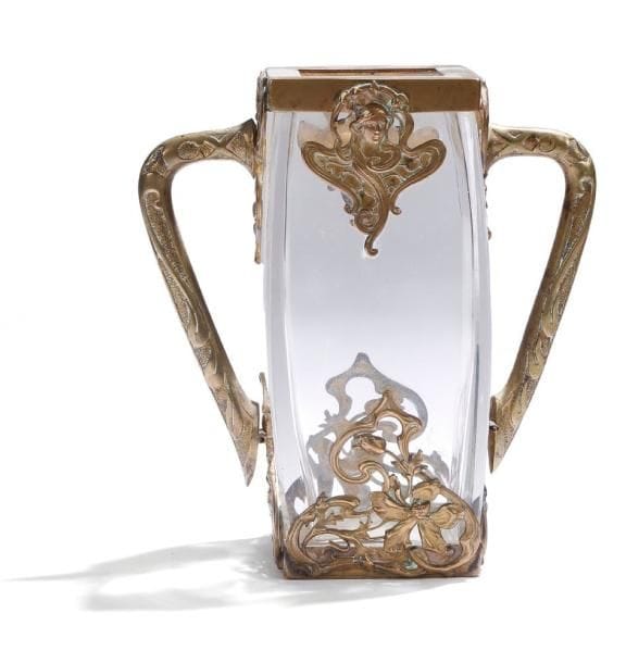 Travail ART NOUVEAU
Précieux vase en cristal enchâssé dans une monture en bronze et laiton doré aux motifs floraux et figurant des visages féminins.  Anses détachées au décor géométrique.  Hauteur : 15,5 cm