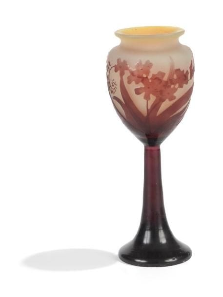 Émile GALLÉ (1846-1904)
Vase calice sur haut pied et au col étranglé annulaire.  Épreuve de tirage industriel en verre multicouche dégagé à l'acide au décor aubergine, de montbrétias, sur fond jaune opalescent.  Signé GALLE en réserve gravé en camée à l'acide.  Hauteur : 20 cm