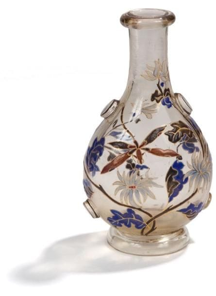 Émile GALLÉ (1846-1904)
Vase en bouteille persane reposant sur une base circulaire en doucine.  Épreuve en verre très légèrement fumé au décor tournant émaillé polychrome et rehaussé à l'or d'une libellule survolant des fleurs sauvages.  Les parties latérales sont ornées de quatre cabochons en verre.  Signé E. GALLE Nancy gravé sous la base.  Hauteur : 13,5 cm