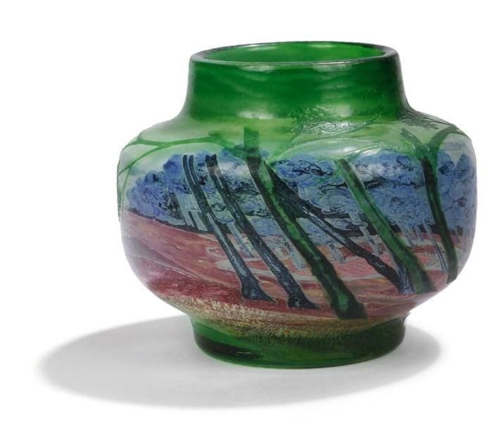 Désiré CHRISTIAN (1846-1907) pour CHRISTIAN Frères & Fils
Forêt au soleil levant, circa 1900. Rare et exceptionnel vase, à panse cylindrique, reposant sur talon et à très large col.  Épreuve en cristal soufflé multicouche vert, blanc et translucide, au décor dans le goût Nabi réalisé en émaux polychromes intercalaires, bleus, verts, lie de vin et noirs.  La couche supérieure est finement gravée d'arbres feuillus, reprenant en superposition et/ou en poursuite le décor interne sur un fond laissant apparaître des parties translucides.  Le soleil, ses rayons et, en partie, le sol ocre sont évoqués par des feuilles d'or éclatées en inclusions.  L'ensemble de la partie figurative, le dessous de la base et le pourtour du col sont entièrement repris à la roue et finement martelés, le fond est achevé en polissage.  Signé D. CHRISTIAN Meisenthal Lorraine sous la base.  Hauteur : 14 cm. Diamètre : 16 cm. Bibliographie : . « Verrerie d'Art de Lorraine - Désiré Christian » par Philippe Olland. Éditions Faton. Dijon 2010. oeuvre reproduite page 143.  .  Désiré CHRISTIAN et émile GALLé, deux destins croisés. . Remarqué dès 1867 par Emile Gallé, alors en charge de la direction artistique des affaires de son père Charles, Désiré Christian est un jeune décorateur à l'émail à la verrerie Burgun, Schverer & Cie. Gallé l'engage dès lors à temps partiel pour son propre compte au sein de la manufacture de Meisenthal et débute ainsi une histoire en parallèle de deux des figures centrales de l'art du verre en France de la fin du XIXe siècle.  . Dix ans plus tard, l'artiste phare de ce qui deviendra l'Ecole de Nancy, promeut Désiré Christian responsable de l'atelier de décoration qui lui est exclusivement dédié.  . En 1885, un accord (secret) est conclu entre Gallé, Mathieu, Burgun et Christian, définissant le rôle de chacun dans la production de verreries artistiques. . . L'année 1889 voit Emile Gallé devenir actionnaire de la Société Burgun, Schverer & Cie alors que celle-ci étend son activité.  . La verrerie de Meisenthal commence à développer s