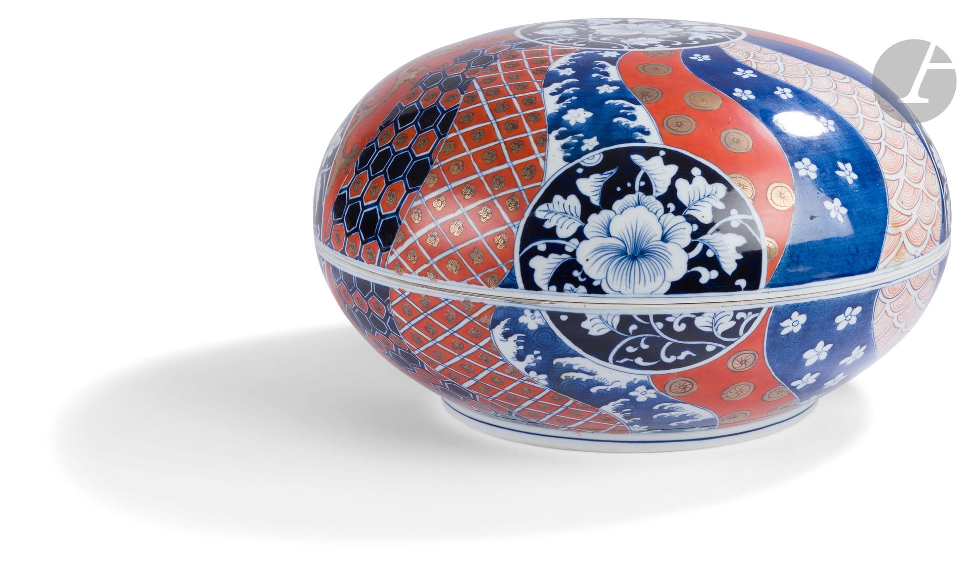 Japan 
Large covered porcelain bowl with blue, red and gold Imari decoration of peonies in medallions and bands imitating fabric with alternating motifs of waves, flowers, foliage and trellis on a blue and red background. 
19th century.  
L. 37 cm.