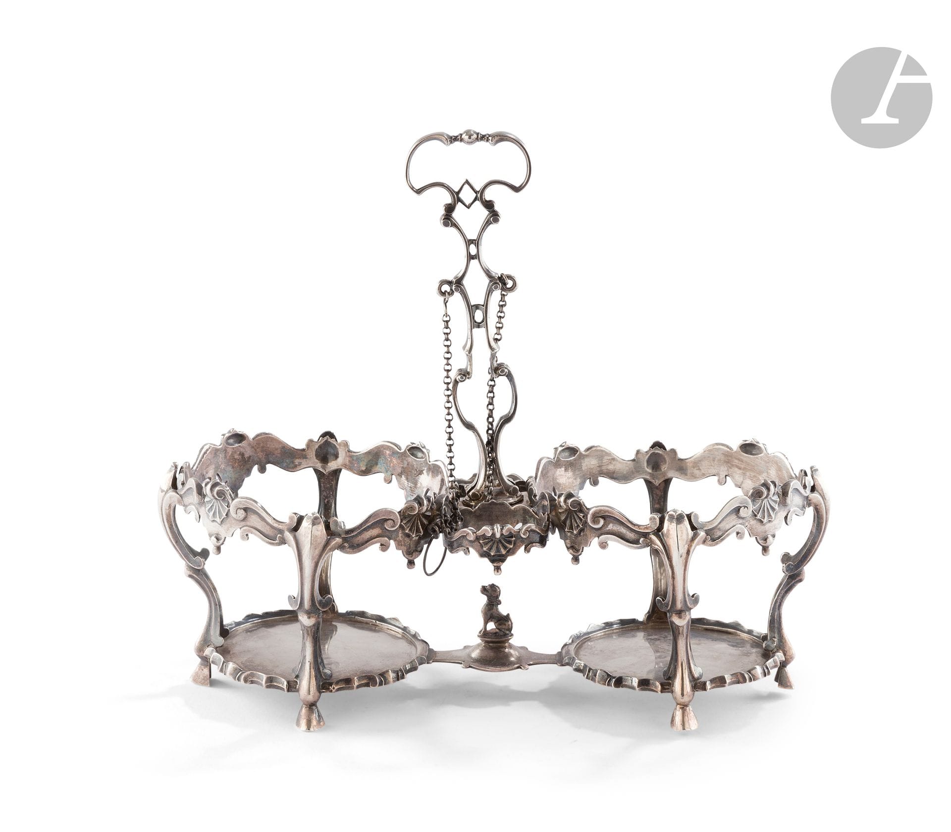 VILLE DE MONS 1767 - BELGIUM
Silver oil and vinegar cruet stand on four sabot feet, the rocaille mounting embellished with shells and scrolls. The openwork, curved and counter-curved central socket is terminated by a central socket. The base features a dog in the round on a small console.
Master goldsmith: an unidentified heart.
Weight : 447 g - length : 22.5 cm - height : 20.5 cm
Condition : the end of one of the two chains is missing.