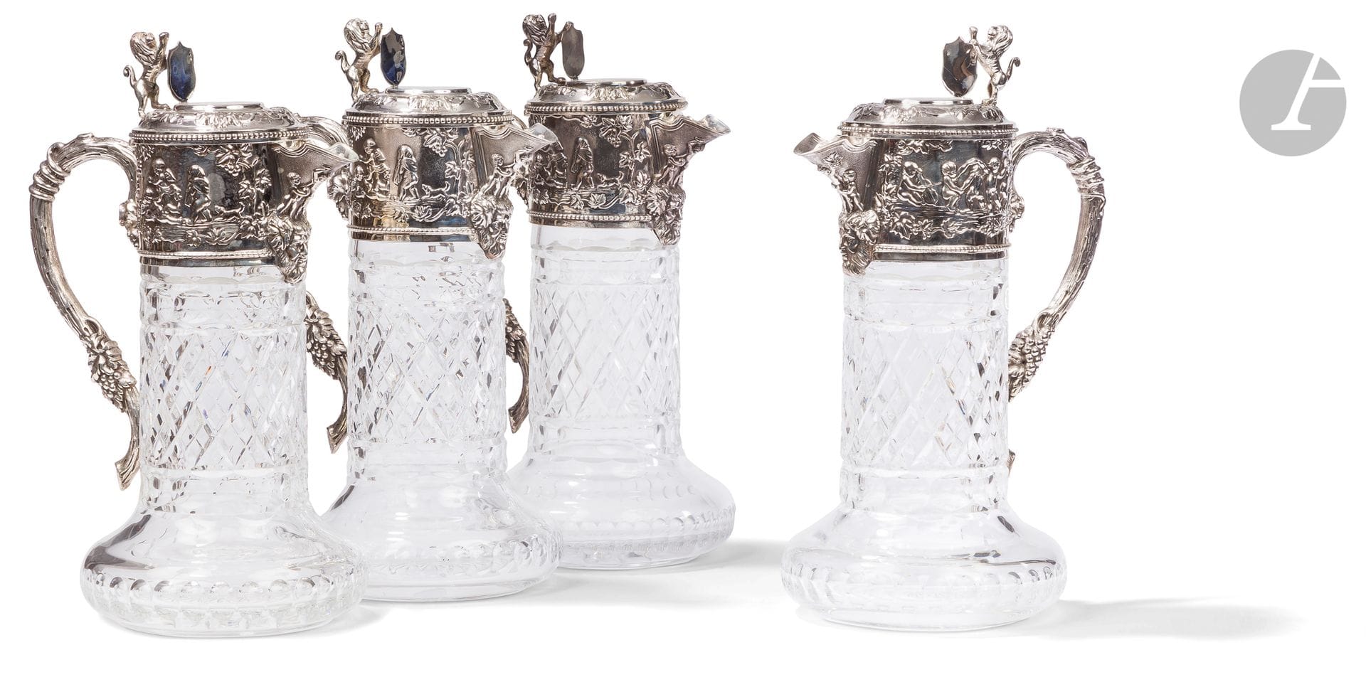 PORTUGAL - PORTO XXe siècle
Ensemble de quatre aiguières en cristal taillé et monture en argent 925 ‰. De forme circulaire, le cristal reçoit dans sa partie supérieure une frise repoussée sur deux faces de scènes figurant des putti dansant et jouant encadrant un bec verseur souligné d'une tête de Bacchus, et une anse à l'imitation d'un cep de vigne. L'appui-pouce du couvercle à charnière figure un lion héraldique tenant un blason dont le champ est laissé vierge de gravure.
Orfèvre : TOPAZIO
Poids brut : 6883,6 g - hauteur : 28,5 cm - diamètre de la base : 13,5 cm