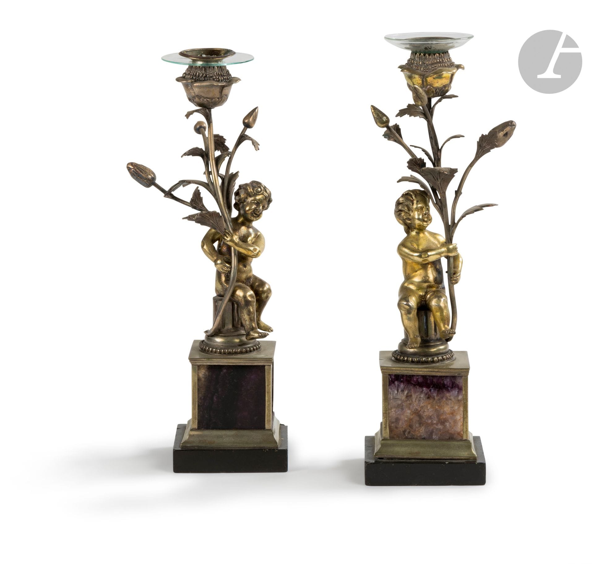 Paire de flambeaux en bronze et laiton argenté, à décor d'un enfant assis sur un fût de colonne tenant un bouquet, reposant sur une base quadrangulaire à plaque d'améthyste ; (accidents et usures).
Probablement Italie, fin du XVIIIe siècle.
H. 32,5 cm