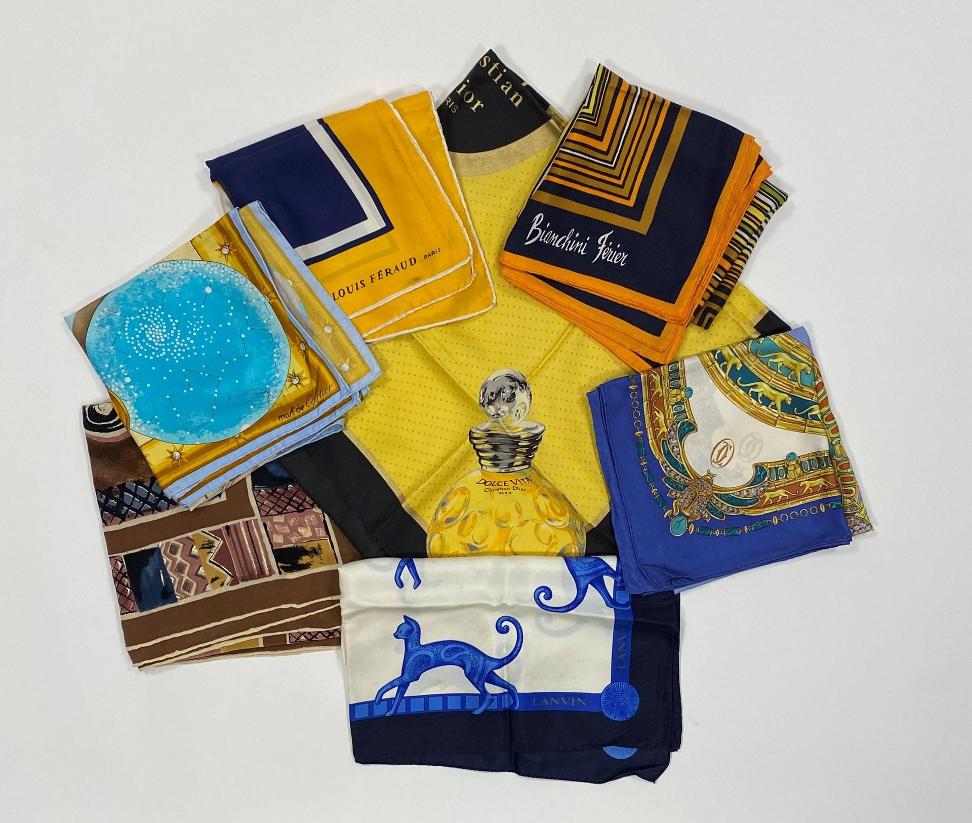 Seven silk twill scarves: a La Dolce Vita by Christian DIOR, yellow background with black surround, a Bianchini FERIER with stripes, a Louis FERAUD cream and navy yellow (soiled and stained), a CARTIER, a Must de CARTIER (heavily stained), a LANVIN with blue cat design, a Pierre CARDIN shawl.