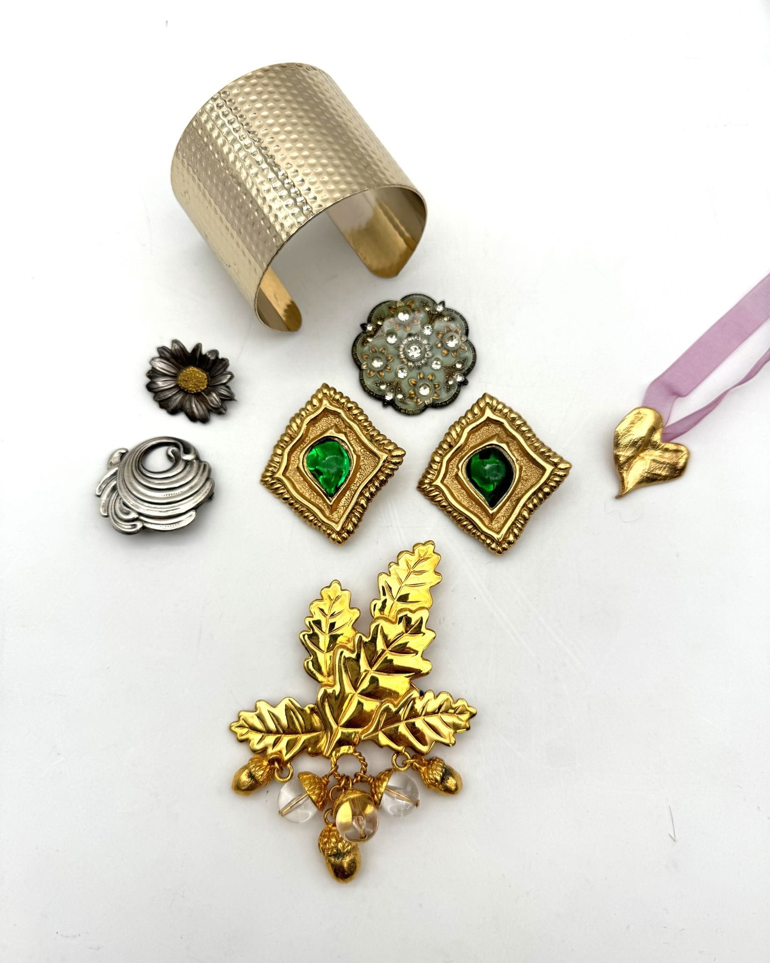 Lot de bijoux fantaisie dont un bracelet manchette en métal doré Jean Paul GAULTIER Classique, une paire de clips d’oreilles SCHERRER en métal doré et pierres vertes, une broche feuilles de chêne Inès de la Fressange, on y joint trois broches et un pendentif coeur