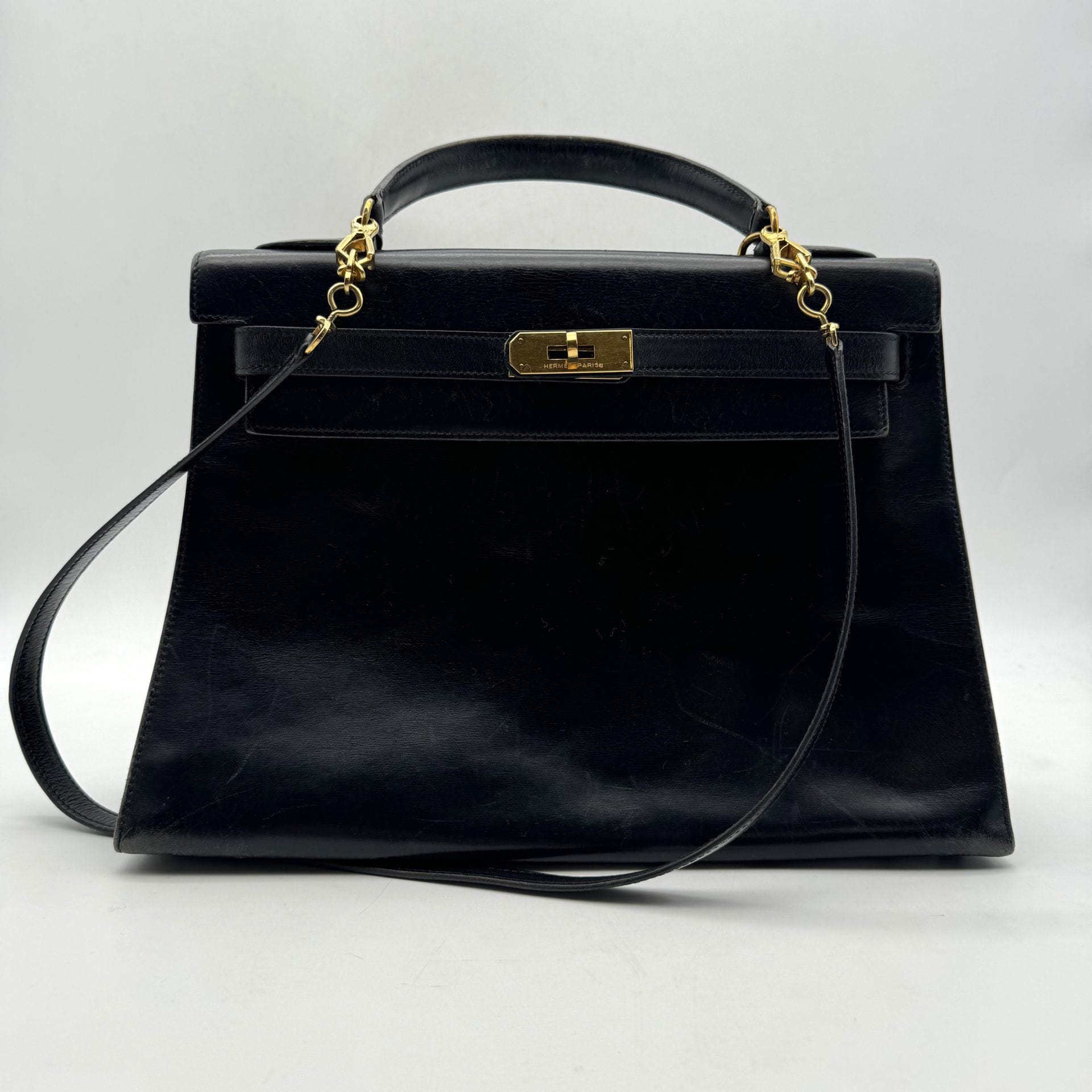 HERMÈS Paris Made in France
Sac Kelly sellier 32 en box noir, garniture en métal doré, bandoulière, cadenas et deux clés sous clochette, housse. Année 1988. 32,5 x 23 x 11,5 cm. (Usures aux angles, rayures et quelques traces)