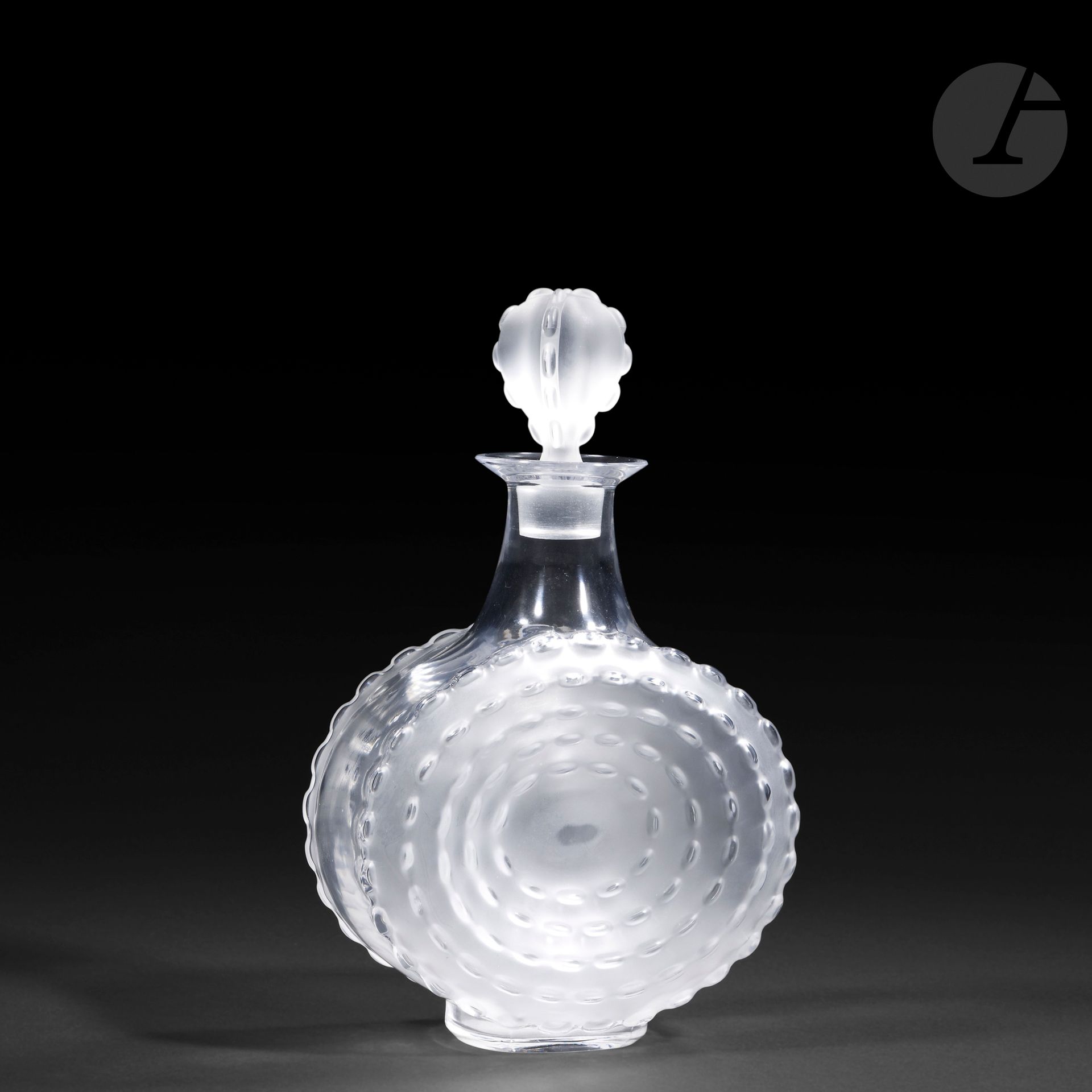 MARIE-CLAUDE LALIQUE (1935-2003) – MAISON LALIQUE
Parme
Carafe méplate à petit col achevé évasé; le bouchon en graine.
Épreuve en cristal moulé-pressé pour la base et soufflé-moulé pour le bouchon et, en partie, satiné. 
Non signée.
Hauteur: 26,5 cm