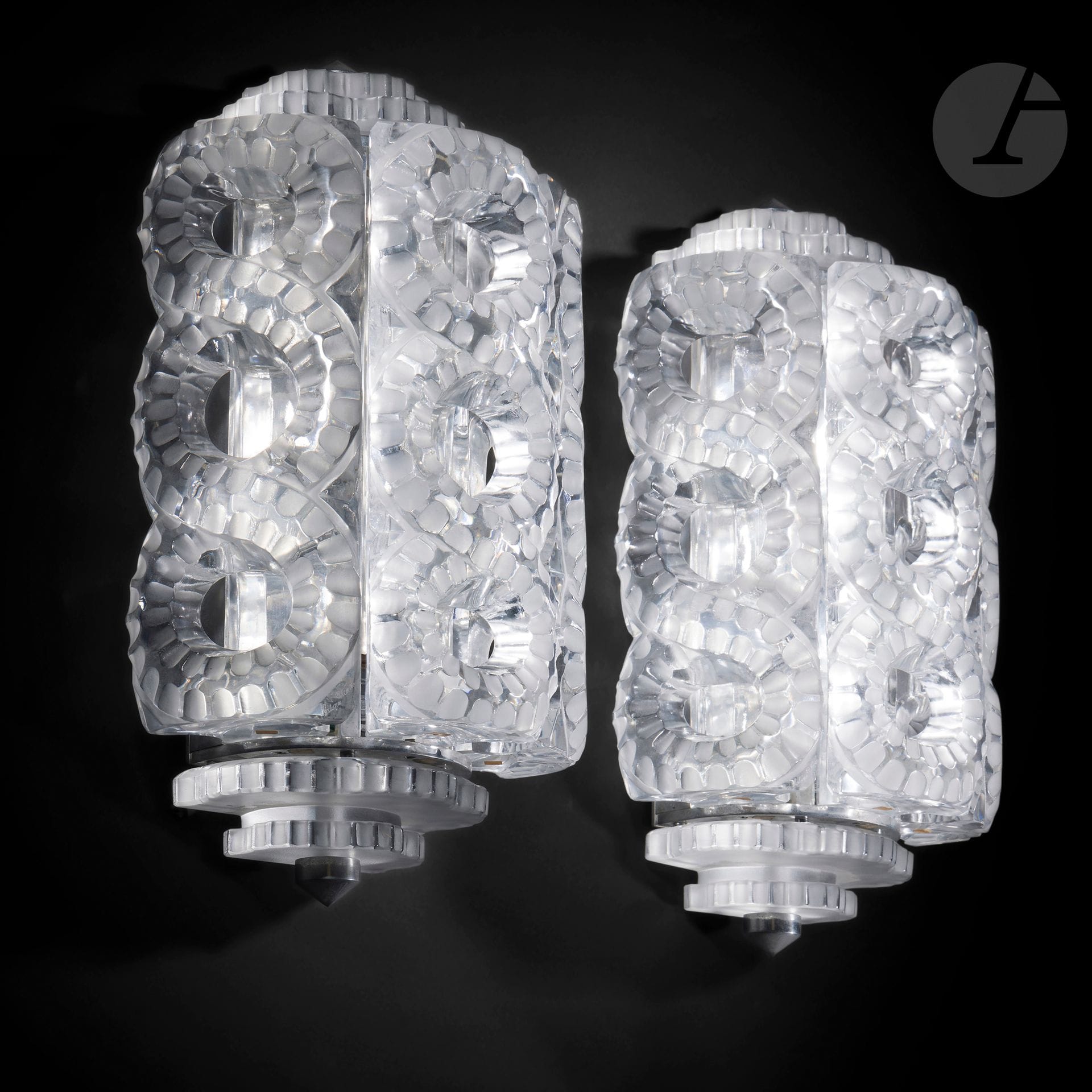 MARC LALIQUE (1900-1977) - MAISON LALIQUE
Séville, small model, the model designed in [1947].
Pair of sconces.
Proofs in molded-pressed crystal, and partly satin-finish; the structures in metal (Ref. Lalique General Catalogue 2012: 1000200). 
Each complete with its upper and lower ends in satin-finish crystal and metal;
Small scattered chips. 
Each sconce signed LALIQUE ® France in cursive letters, at the tip, towards the end of one of the rows. 
Height: 39 cm - Width : 19,5 cm - Depth : 12,5 cm