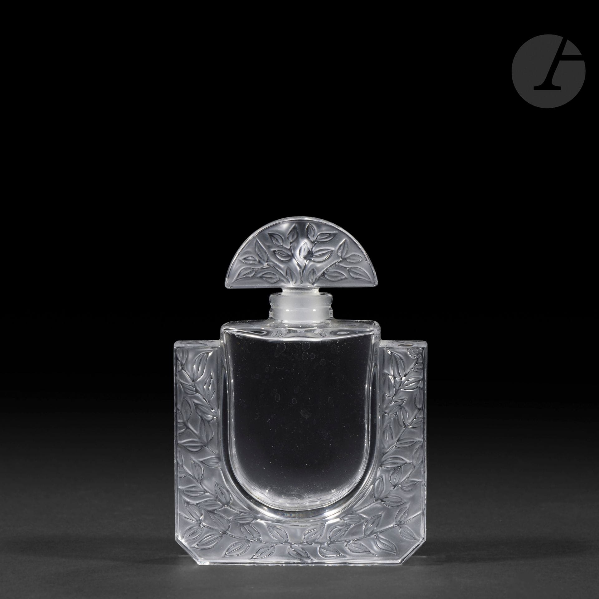 MARIE-CLAUDE LALIQUE (1935-2003) – MAISON LALIQUE (1935-2003)
Chèvrefeuille, le modèle conçu en [1992]
Flacon à parfum, le corps rectangulaire et le bouchon demi-lune au décor de feuilles.
Épreuve en cristal soufflé-moulé pour la base et moulé-pressé pour le bouchon et, en partie, satiné.
Une égrenure sur la base.
Signé LALIQUE ® France en lettres cursive à la pointe vers la base et numéroté E.0421 sous la base.
Hauteur : 11,2 cm