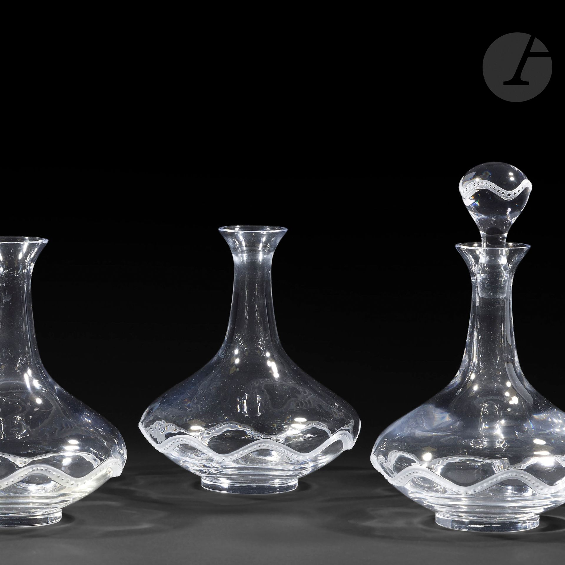 MARIE-CLAUDE LALIQUE (1935-2003) – MAISON LALIQUE
Champs de Mars 
Suite de quatre carafes; une seule complète de son bouchon. 
Épreuves en cristal soufflé-moulé, en partie, satiné ; l’unique bouchon en cristal moulé-pressé, en partie, satiné. 
Un choc sous la base de l’une des carafes; infimes égrenures éparses; manquent 3 bouchons.
Deux carafes signées LALIQUE ® France en lettres cursives, à la pointe sous la base. 
Hauteur :20 cm 
Hauteur de la carafe avec bouchon: 25 cm