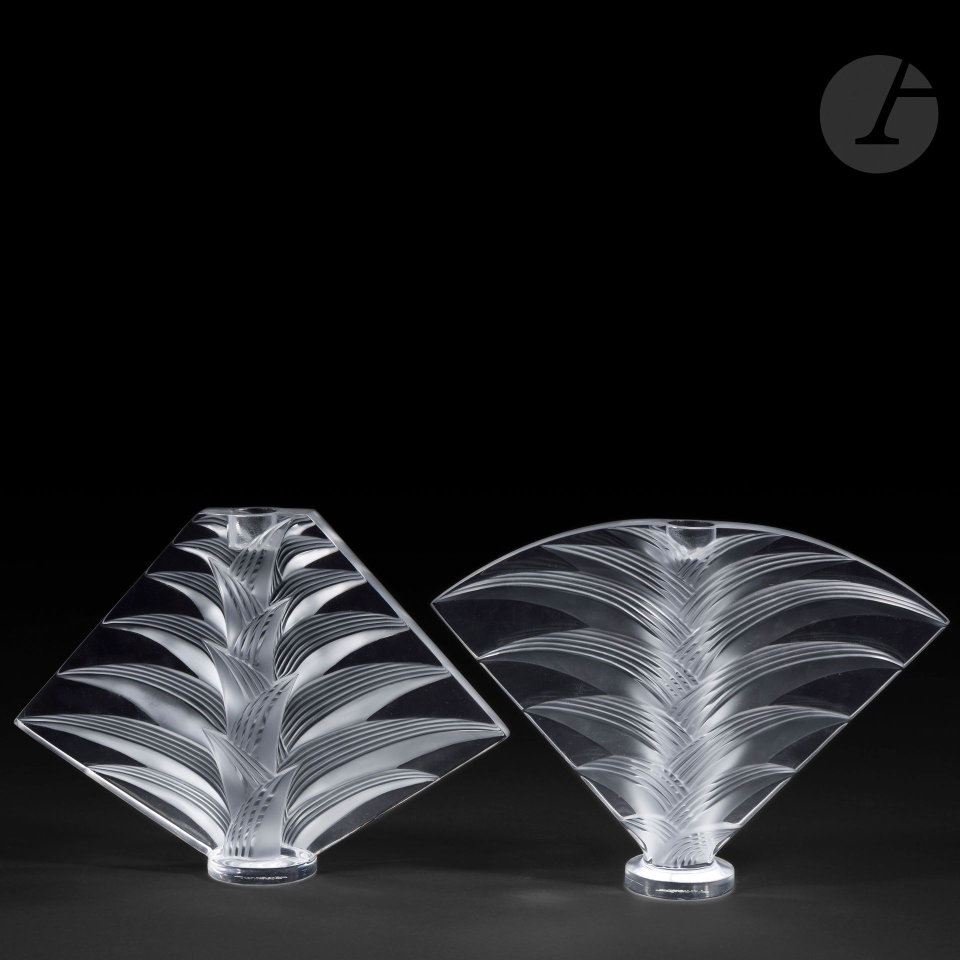 LALIQUE HOUSE 
Ravelana
Pair of candleholders; one diamond-shaped, the other fan-shaped, each resting on a circular base. 
Proofs in molded-pressed and, in part, satin-finished crystal.
A chip at the right end of the diamond-shaped candlestick, small scratches under the bases. 
Each signed LALIQUE ® France in cursive letters, at the point, under the base. 
Height: 20.5 cm - Length: 27.5 cm