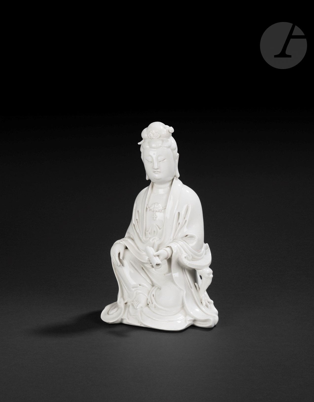 Guanyin en porcelaine blanc de Chine, Chine, Dehua, XVIIIe siècle
Représentée assise, vêtue de robes superposées tombant en plis autour du corps, le torse paré d’un collier de perles et d’un pendentif en forme de fleur de lotus. Le visage est serein, les yeux baissés et les cheveux sont rassemblés en un chignon coiffé d’épingles. Le front est paré de l’urna et les lobes d’oreille sont allongés. Le bras gauche est posé sur un accoudoir au plateau incurvé reposant sur un pied à tête de dragon terminé par une patte de dragon à quatre griffes accrochée au vêtement. La main gauche tient un rouleau. Le pied droit nu dépasse du bas de la robe. Dans le dos figure une marque carrée moulée, difficilement identifiable. Couverte légèrement craquelée.
Hauteur : 24 cm
