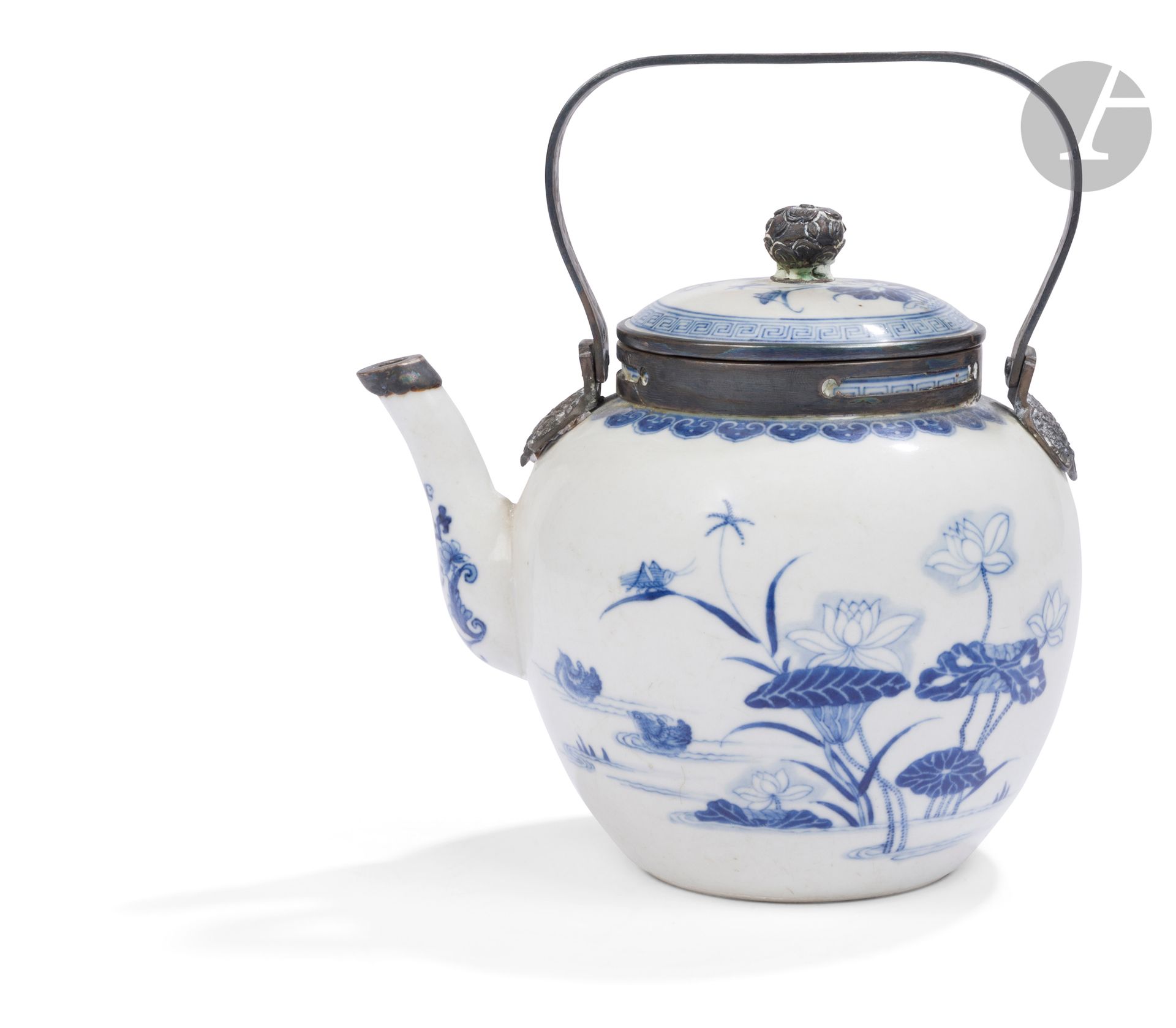 Théière en porcelaine bleu-blanc, Chine pour le Vietnam, XIXe siècle
La panse sphérique est décorée en bleu sous couverte de deux canards mandarins sur un étang entouré de fleurs, feuilles de lotus et d’un insecte. Au niveau du col, une frise de tête de ruyi en forme de lingzhi. Le couvercle légèrement bombé est orné du même décor entouré d’une frise de grecques. L’anse est ciselée de rinceaux et de têtes de dragons au niveau de la jonction avec la porcelaine. L’anse, la prise du couvercle ainsi que son cerclage, et celui du bec verseur sont en argent. Sous la base, une marque à deux caractères fāng mào - 芳茂.
Hauteur : 15 cm
Percée pour fixer la monture en argent. Petits fels à l’intérieur du couvercle, petites rayures sur la surface.