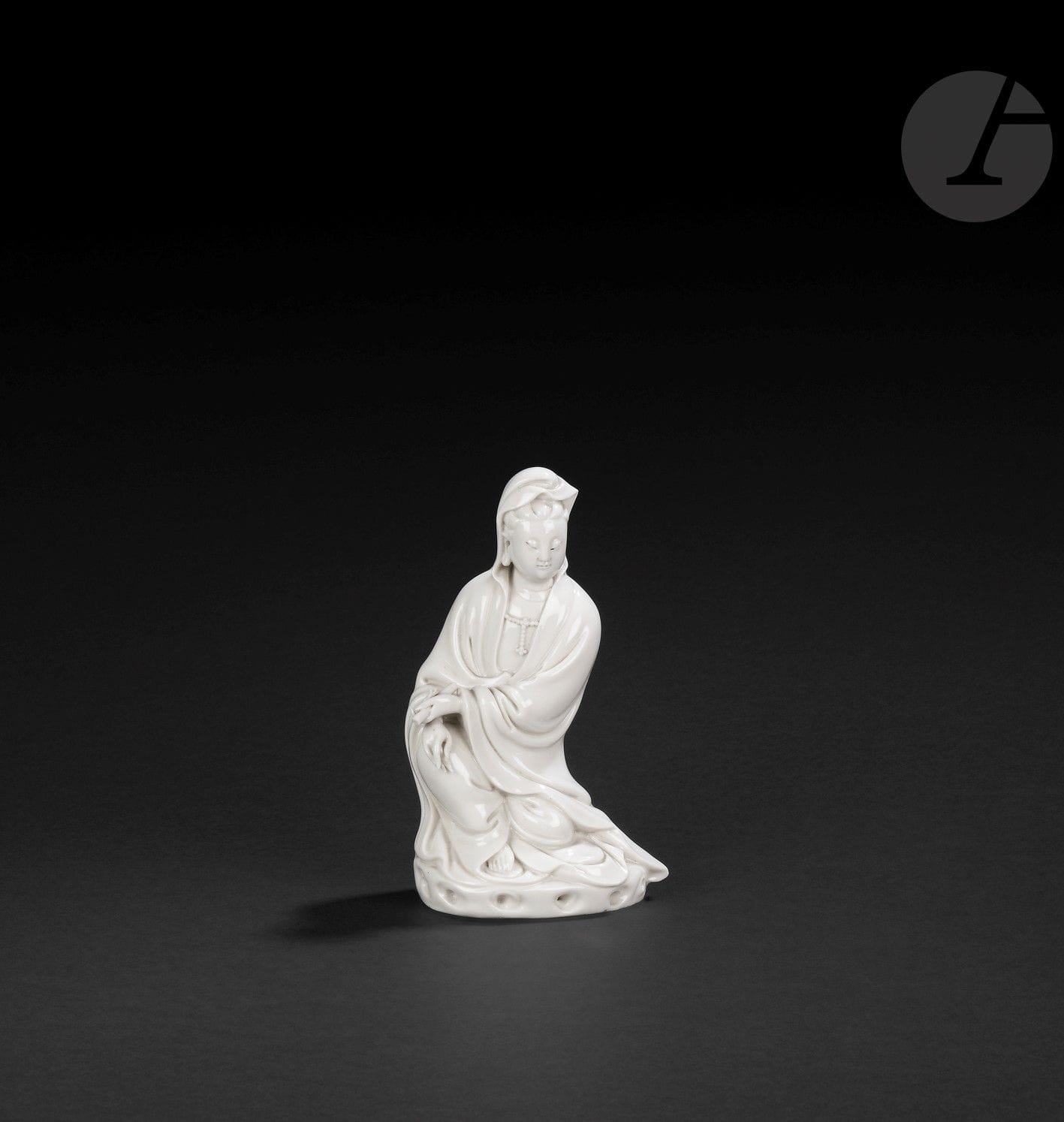 Guanyin in Chinese white porcelain, Dehua, China, 17th - 18th century
Depicted seated on a small base depicting rocks, wearing a long pleated robe open to the chest and adorned with a pearl necklace. Her face is serene, her eyes downcast and her hair covered by the robe. Her forehead is adorned with a central urna, and her earlobes are elongated. She holds a scroll in her left hand. Her bare right foot protrudes from the bottom of her dress. On the back is a molded double-gourd mark, difficult to identify.
Height: 15.5 cm
A broken finger on the left hand.

Provenance: 
E&amp;J Frankel Collection" label.