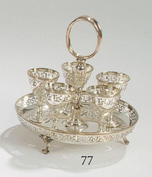 Nécessaire à oeufs, en métal argenté, à cinq coquetiers posant sur un présentoir tripode, l?ensemble à décor ajouré de grecques. (Manque les cuillers). Travail anglais.
