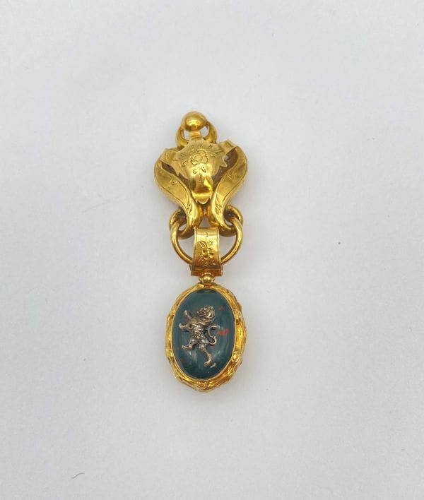 Broche en or 18K (750), retenant un médaillon porte-souvenir en or 18K et jaspe sanguin appliqué d'un profil de lion en argent piqué de diamants taillés en roses, recélant un compartiment avec glace. Travail français de la fin du XIXe siècle. Hauteur : 6,2 cm environ. Poids brut : 13,2 g (manque, déformation)