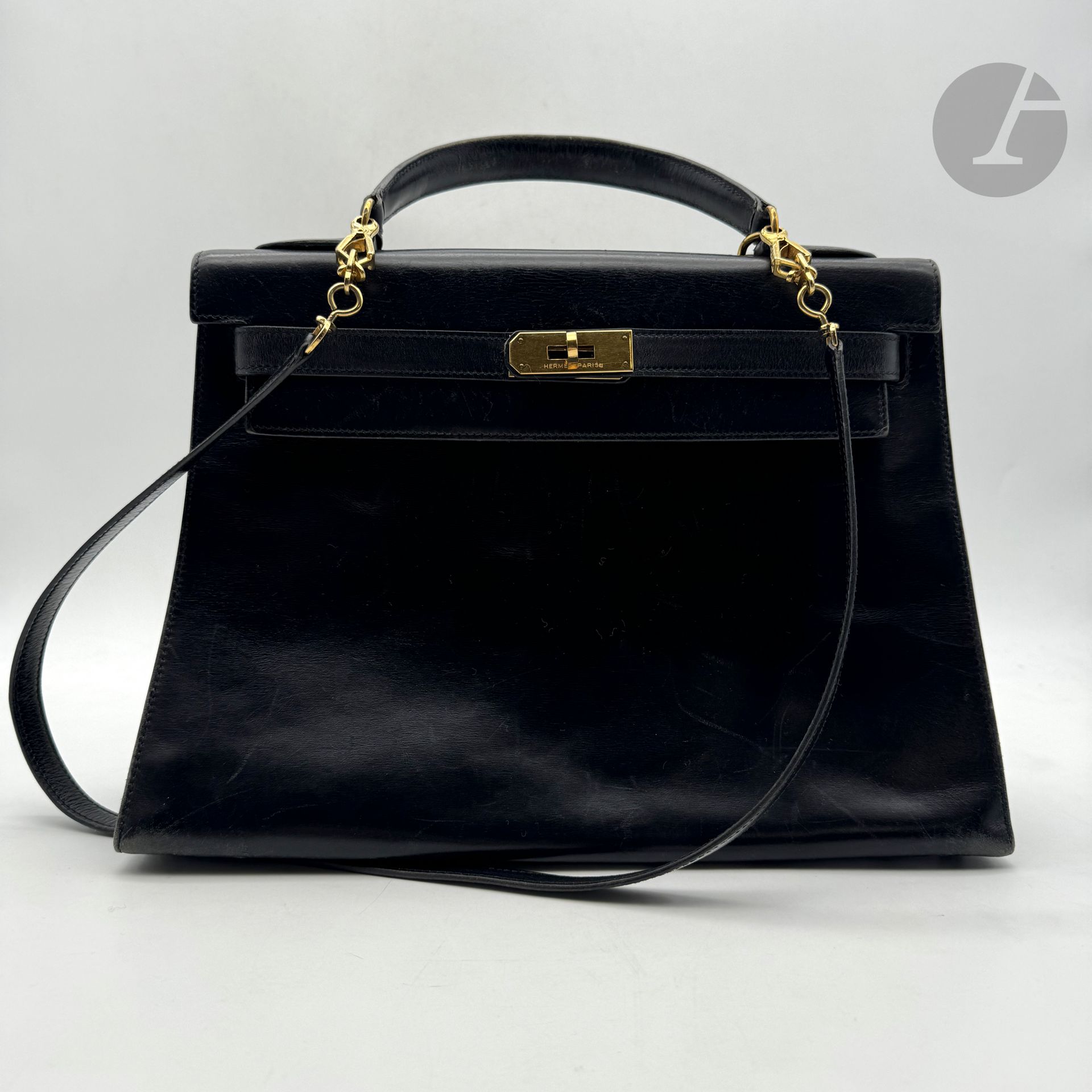 HERMÈS Paris Made in France
Kelly saddle bag 32 in black box, gold metal trim, shoulder strap, padlock and two keys under bell, cover. Year 1988. 32.5 x 23 x 11.5 cm (Worn corners, scratches, a few marks and damaged reel).
