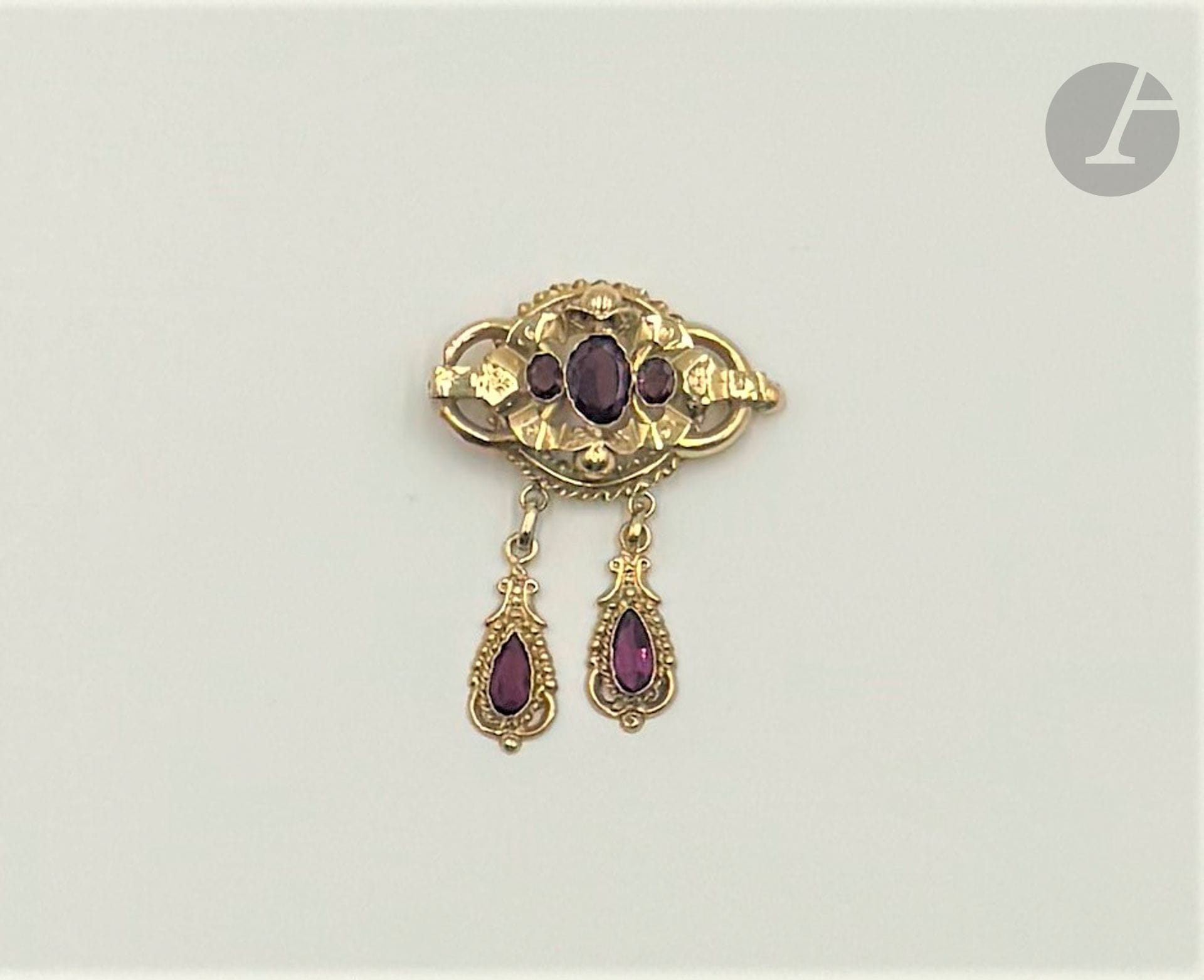 Brooch in smooth, twisted 18K (750) gold, the central motif engraved and set with 3 oval garnets, adorned with two pendants set with fancy violet stones. Dimensions: approx. 5.2 x 4 cm. Gross weight: 6.6 g