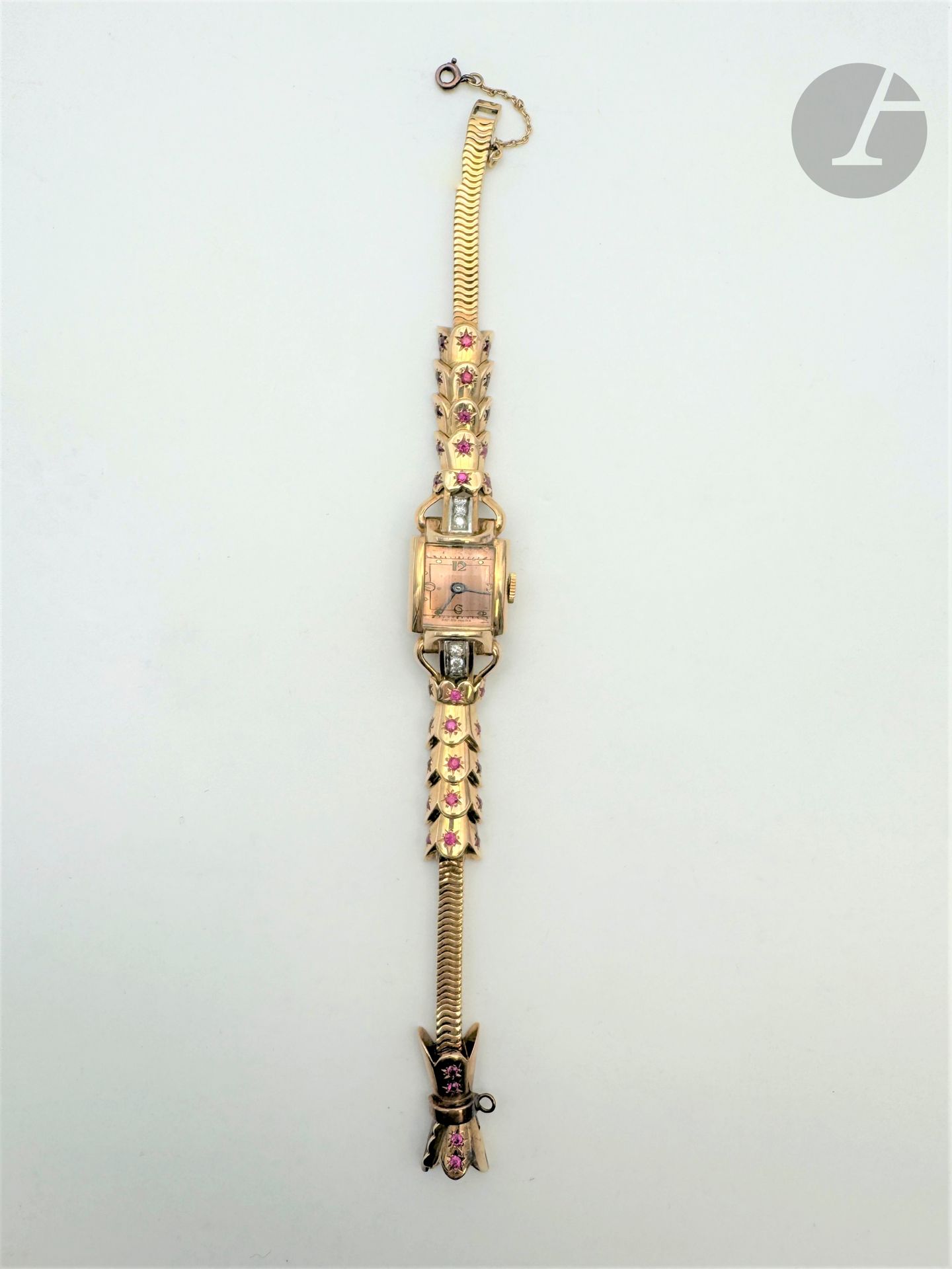 Montre de dame en or rose 18K (750) et platine, le boîtier quadrangulaire bombé, épaulé de diamants ronds taille brillant, le bracelet articulé de maillons en écailles  piquées de rubis dans des étoiles gravées terminé par une maille serpent. Travail français des années 1940. Longueur : 18,5 cm environ. Poids brut : 54,3 g (oxydations, fonctionnement non garanti)