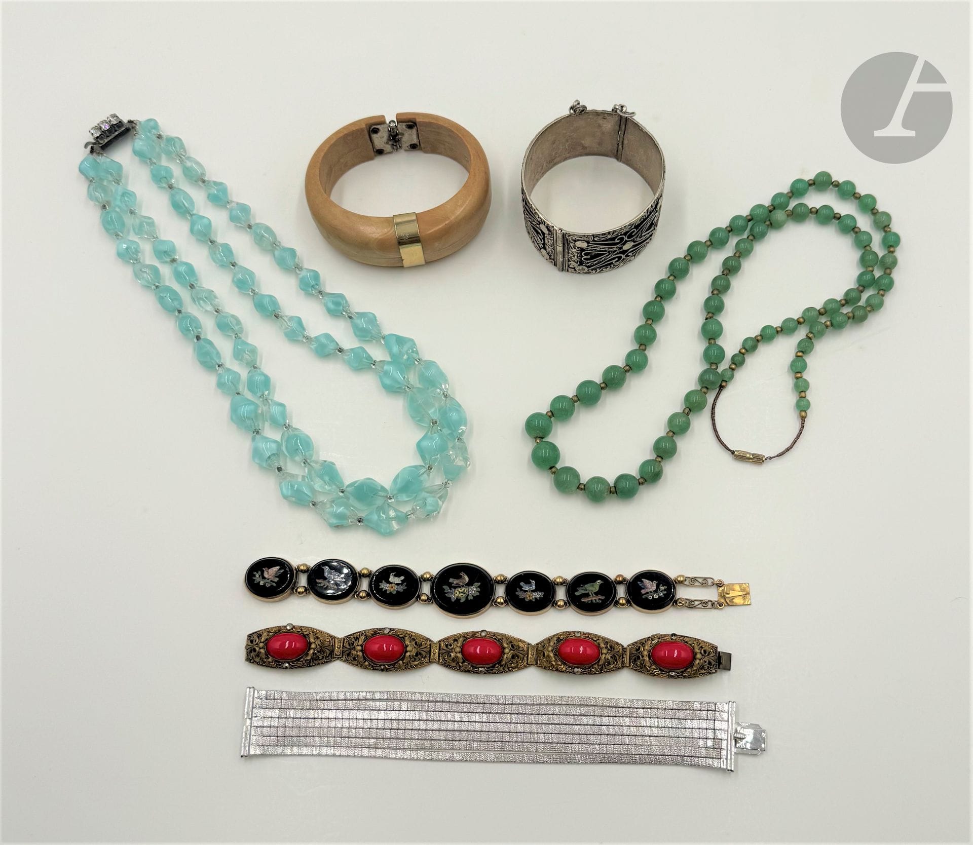 Lot de bijoux fantaisie comprenant : un bracelet ouvrant en argent ciselé, un bracelet en métal doré orné de pierres rouges fantaisie, un bracelet en métal doré agrémenté de 7 micromosaïques polychromes figurant des oiseaux, un bracelet ouvrant en résine et métal doré, un bracelet 7 rangs en métal amati, un collier en verre moulé incolore et bleu et un collier de billes de quartz aventuriné. Poids argent : 64 g (fêles, égrisures, chocs, accidents)