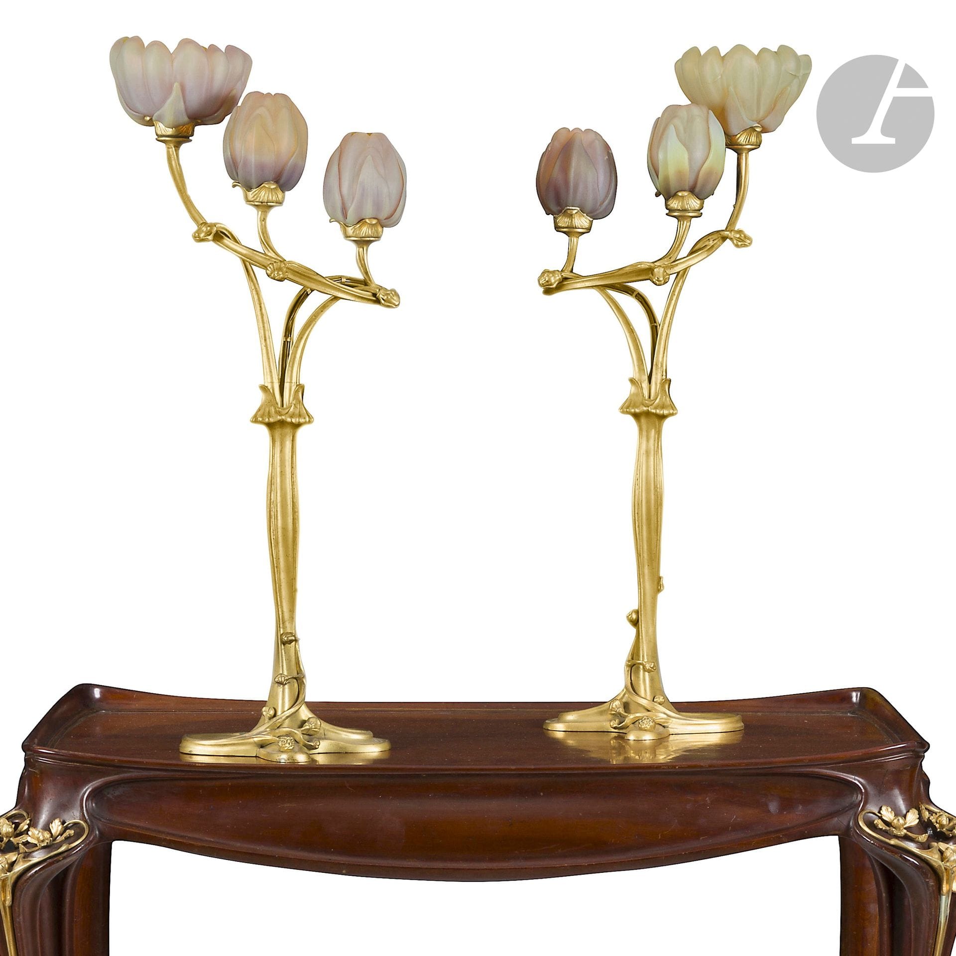 LOUIS MAJORELLE (1859-1926) & DAUM NANCY
Flambeaux à trois lumières Magnolias (droit et gauche) dits improprement Nénuphars,les modèles présentés à l’Exposition de l’École de Nancy, Pavillon de Marsan, Paris, 1903 et au 2ème Salon des Industries du Mobilier, Grand-Palais des Champs-Élysées, Paris, 1905
Rare et exceptionnelle paire de lampes de table, droite et gauche, dites Flambeaux à trois lumièreset formant pendants.
Les pieds, figurant des branches et des bourgeons de type Titre en bronze doré d’origine.
Les cache-ampoules figurant, sur chaque luminaire, une fleur épanouie et deux fleurs avant éclosion totale, en verre soufflé-moulé jaune anisé nuancé d’ambre et repris très finement en gravure à froid.
Époque Art nouveau.
Usures et altérations à la dorure des pieds en bronze, rééléctrification des deux lampes. Sur le flambeau droit: deux accidents et manques et deux cheveux (dont un très long) sur le cache-ampoule le plus grand (fleur épanouie), une fêlure de bas en haut et deux cheveux (dont un long) sur le cache-ampoule du milieu. Sur le flambeau gauche: cinq cheveux (environ 2 à 3cm) sur le cache-ampoule le plus grand (fleur épanouie), quelques rares infimes égrenures (têtes d’épingle) en pourtour des deux autres cache-ampoules.
Chaque verrerie signée DAUM Nancy à la Croix de Lorraine, en gravure vers la base.
Chaque lampe: Hauteur: 85cm – Longueur: 35,5cm

Historique: Provenant initialement d’une entière décoration réalisée par Louis Majorelle pour l’hôtel particulier d’un proche qui fut une grande personnalité lorraine.

Expositions:
- Exposition Lorraine - L’École de Nancy, Pavillon de Marsan à Paris,1903 - Une paire de lampes identiques à notre paire de Flambeaux à trois lumières Magnolias présentée lors de cette manifestation.
- 2ème Salon des Industries du Mobilier, Grand-Palais des Champs-Élysées, Paris, 1905 – Une paire de lampes identiques à notre paire de Flambeaux à trois lumières Magnolias présentée lors de cette manifestation.

Collections publiques:
- Musée de l’École de Nancy, Nancy – Une paire de lampes identiques à notre paire de Flambeaux à trois lumières Magnolias, aux variantes de couleurs pour les cache-ampoules, est conservée dans les collections de cette institution sous les numéros d’inventaire482 et 483.
- Musée d’Orsay, Paris – Un modèle identique à l’un de nos Flambeaux à trois lumières Magnolias, incomplet des cache-ampoules et improprement titré Nénuphar, est conservé dans les collections de cette institution sous le numéro d’inventaire OAO1504.
- Musées royaux des beaux-arts de Belgique, Bruxelles – Un modèle identique à l’un de nos Flambeaux à trois lumières Magnolias est conservé dans les collections de cette institution sous le numéro d’inventaire GC 073. 
- Virginia Museum of Fine Arts, Richmond, USA - Un modèle identique à l’un de nos Flambeaux à trois lumières Magnolias est conservé dans cette institution sous le numéro d’inventaire 2015.309.

Bibliographie:
- Exposition Lorraine - L’École de Nancy au musée de l’Union Centrale des Arts Décoratifs, Pavillon de Marsan à Paris, 2ème Série: Objets d’Art - Verrerie - Céramique - Cuirs d’Art - Bronze - Peinture décorative – Éditions Armand Guérinet, Paris, 1903. Un modèle identique à l’un de nos Flambeaux à trois lumières Magnolias reproduit planche 7.
- Le Salon des Industries du Mobilier, 1905, Grand-Palais des Champs-Élysées, Deuxième volume – Éditions Librairie d’Art Décoratif Armand Guérinet, Paris, 1905. Une paire de lampes identiques à notre paire de Flambeaux à trois lumières Magnolias reproduite planche 207.
- Appareils pour l’électricité – Majorelle à Nancy – Planche imprimée en phototypie par Bergeret, Nancy, vers 1925. Un modèle identique à l’un de nos Flambeaux à trois lumières Magnolias reproduit sous le numéro 4.
- Majorelle – Nancy – Catalogue commercial, vers 1908-1910. Une paire de lampes identiques à notre paire de Flambeaux à trois lumières Magnolias reproduite à plusieurs reprises (isolément et en situation) dans cette publication sans pagination.
- Théodore Lambert (dessins et relevés) – Décorations et ameublements – Intérieurs – Éditions de la Librairie Générale de l’Architecture et des Arts Décoratifs, vers 1905. Une paire de lampes identiques à notre paire de Flambeaux à trois lumières Magnolias reproduite planche 17.
- Maurice Rheims – L’Art 1900 ou le Style Jules Verne – Éditions Art et Métiers Graphiques, Paris, 1965. Un modèle identique à l’un de nos Flambeaux à trois lumières Magnolias reproduit sous l’illustration n°426 (sans pagination).
(Bibliographie complète reproduite au catalogue PDF).
