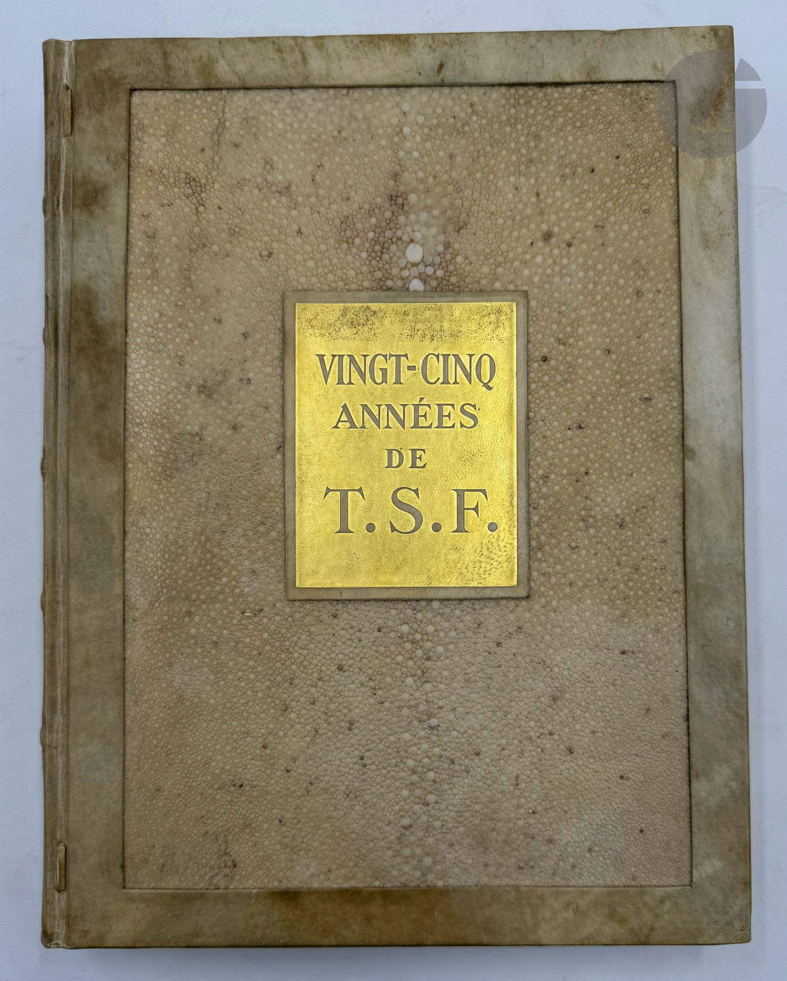 [TSF].
Vingt-cinq années de T.S.F.
S.l. : Société française radio-électrique, [1934]. — In-4, parchemin ivoire encadrant sur les plats une grande pièce de galuchat ivoire, plaque dorée portant le titre au centre du premier plat, dos à faux nerfs orné de filets dorés, tête dorée, non rogné, étui (Jean Duval). 
Superbe ouvrage commémoratif, publié à l’occasion de 25e anniversaire de la création la Société Française Radio-électrique. Il comprend un beau portrait d’Émile Girardeau, fondateur de la société, tiré en sépia, plusieurs centaines de graphiques, statistiques et photos ainsi que 3 étonnantes et belles planches en couleurs sur aluminium, dont une à double page.
Très bel exemplaire dans une reliure originale en galuchat de René Duval, spécialement imprimé pour monsieur Germain-Martin, ministre des finances et ancien ministre des P.T.T.
Quelques rares rousseurs, sans gravité.