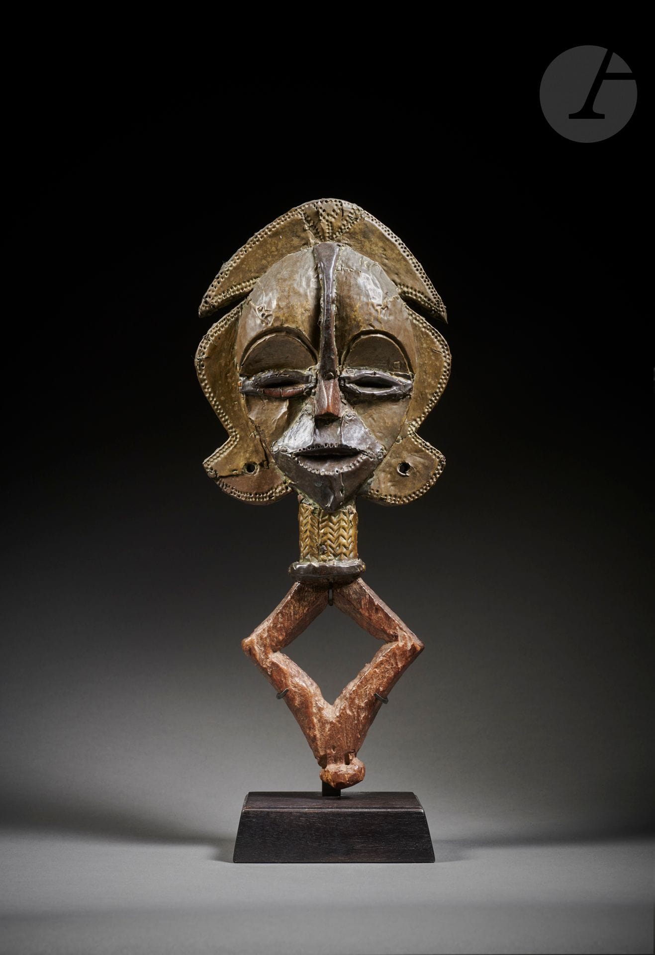 Une figure de reliquaire mbulu ngulu.
Aussi appelée mboy ou omboye en pays Kota, la figure de reliquaire de la collection Jean Roudillon est un superbe exemple classique de l’art des Kota Obamba ou Bawumbu. Présentant un visage aux volumes concaves et convexes, utilisant deux couleurs de métal, cette figure de reliquaire vient enrichir le corpus entrant dans la catégorie numéro neuf selon la classification de l’ouvrage de référence dit « le Chaffin » L’Art Kota Les Figures de Reliquaire, et dont on retient un exemplaire assez proche dans les collections du British museum de Londres et aussi le fameux kota aux yeux ronds de la collection Barbier-Mueller. Ici la bouche ouverte très expressive, comme chantante, est ornée de petits points sur tout son contour, et de la même manière sur l’ensemble du pourtour sur le croissant et les ailettes. à l’arrière le losange est sculpté avec souplesse et traversé d’une barre verticale sculptée en relief, légèrement convexe, témoignant aussi d’un très beau style ancien.
Jean Roudillon, très attaché à cette œuvre qui provenait de l’ancienne collection Albert Sarraut, avait commandé à Louis Perrois une étude pour cette superbe figure de reliquaire que les connaisseurs savent d’un style ancien, même archaïque, et de surcroît ici très bien conservée. L’étude de Louis Perrois, très bien documentée, compare cette œuvre à d’autres figures de reliquaires dans les anciennes collections de Paul Guillaume, Helena Rubinstein, Arman, Madeleine Rousseau ou George Gershwin.
Dans les notes de Jean Roudillon : 
« Afrique, Gabon, Kota
Figure reliquaire en bois recouvert de feuilles de laiton et de cuivre.
Ancienne collection Albert Sarraut, ministre des Colonies d’un gouvernement de la IIIe république.
Exposé à l’international sporting club de Monte Carlo, Antiquaires et Galeries d’Art du 25 juillet au 11 aout
1975 et reproduit au catalogue p. 73 ».
Kota Obamba ou Bawumbu, Gabon
Bois, laiton, cuivre rouge, usures et érosion d’ancienneté, très belle et ancienne patine d’usage.
H. : 37 cm
Voir p. 146 à 158 pour la catégorie 9 dans : Art Kota Les Figures de Reliquaires, Alain et Françoise Chaffin, Ed. Chaffin Meudon 1979
Voir : une étude de Louis Perrois commandée par Jean Roudillon et remise à l’acquéreur.
Provenance :
- Collection Albert Sarraut (collecté dans les années 1920)
- Collection Jean Roudillon (acquis à Paris dans les années 1950)
Exposition et publication :
Première exposition internationale des antiquaires et des galeries d’art, Sporting Club de Monte Carlo, du 25 juillet au 11 août 1975, reproduit au catalogue p. 73.