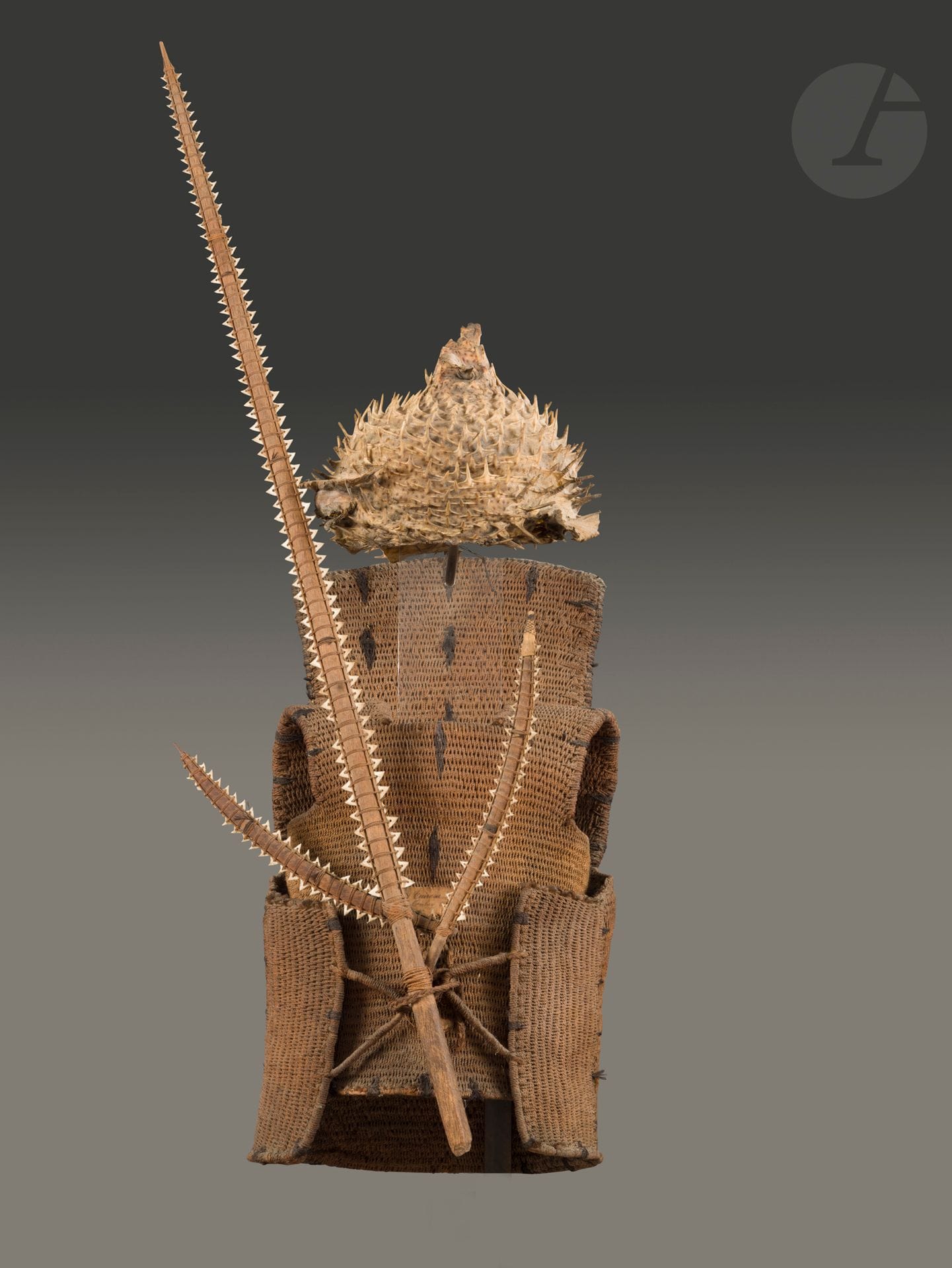 A te otanga warrior's cuirass from a bwai ni buoka armor with helmet and saber-trident.
From an old collection of which a fragment of the label survives with a probably erroneous attribution, it is very rare to find these emblematic Kiribati fighting armors with their helmet made from the dried skin of the porcupine fish (Diodon holocantus).
Republic of Kiribati, formerly Archipelago Islands
Gilbert
Braided coconut pericarp fibers, human hair, remnant of an old collector's label, porcupine fish skin, wood fiber and palm leaves, shark teeth, minor accidents, very fine oxidation and old patina.
H. of armor: 73.5 cm, H. of saber-trident: 126 cm
Provenance :
Jean Roudillon