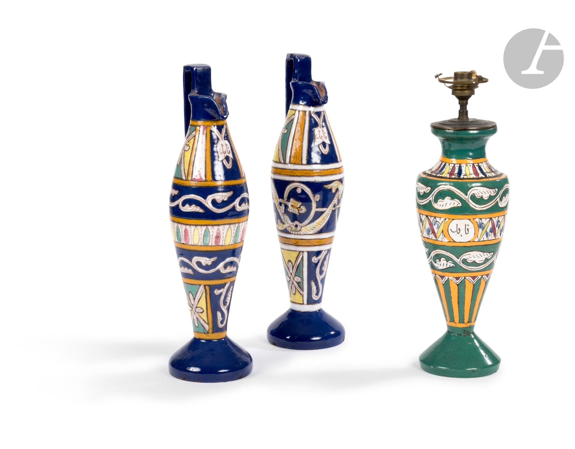 Paire d’aiguières chianti et vase monté en lampe dans le goût de Tissier, Tunisie, Nabeul, XXe siècle
Deux verseuses à panse fusiforme sur piédouche convexe, la lèvre pincée et l’anse angulaire, le vase de forme balustre. En faïence polychrome, les aiguières à dominante bleue, le vase à dominante verte, chaque pièce présentant un décor en plusieurs registres renfermant des motifs végétaux et géométriques ainsi qu’un médaillon inscrit en arabe “Nabeul”.
Hauteur : 40 cm ; 39,5 et 32,5 cm (sans la monture)
Légères égrenures, montage électrique sur le vase rempli de graviers ou de sable.

A Pair of Tall Pottery Ewers Chianti and a Vase, Tunisia, Nabeul, 20th century