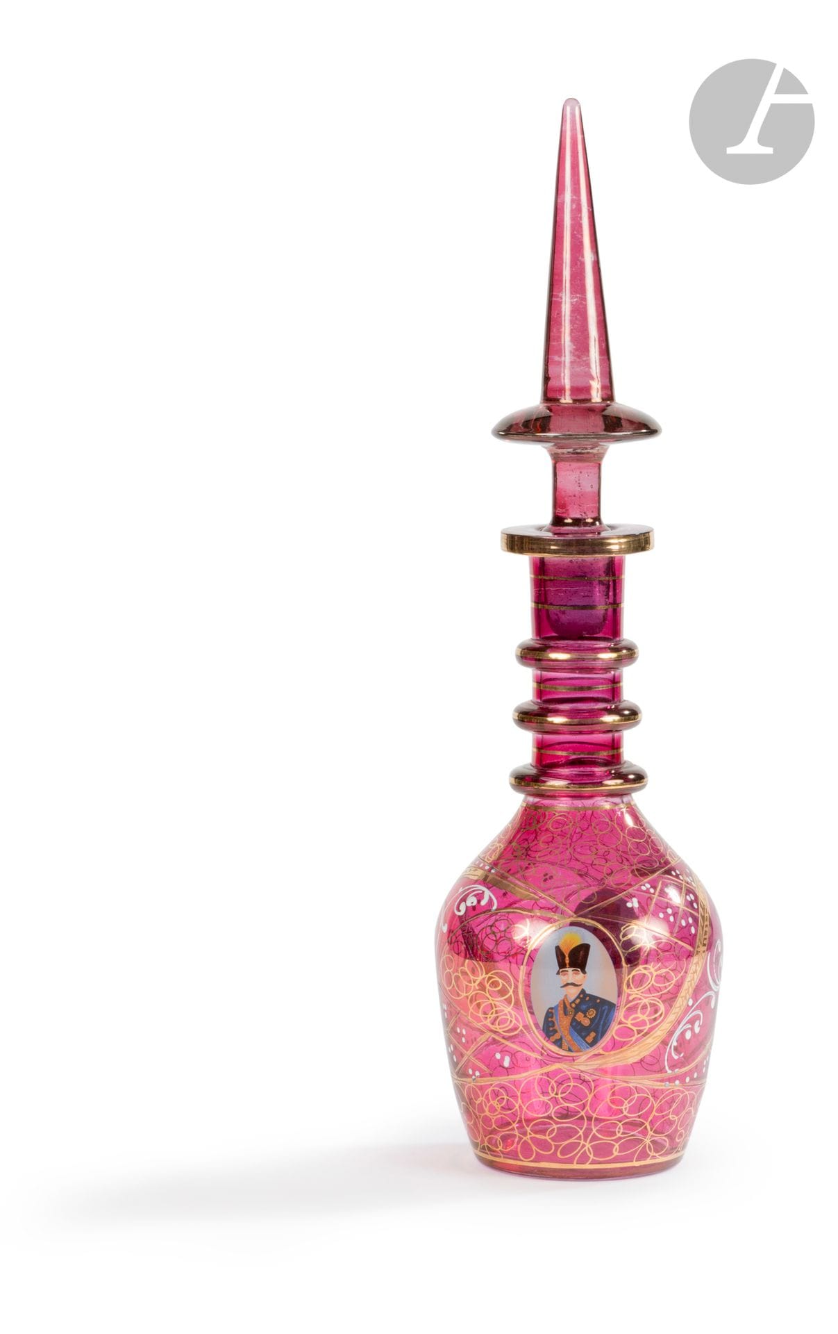 Carafe à l’effigie du roi Nâser ed-Din Shâh Qâjâr (r. 1848-1896), Bohême pour l’Iran, XXe siècle 
En verre transparent de teinte grenat à décor peint en polychromie et doré de deux médaillons ovoïdes renfermant un portrait du Shâh d’Iran Nâser ed-Dîn Shâh en costume de cérémonie avec ses décorations et sa coiffe à aigrette. 
H. totale : 44,7 cm
Petits manques à la base du bouchon, dorure légèrement effacée par endroits.

A Bohemian Glass Bottle and Tapering Stopper with a Portrait Medallion of Nâser ed-Din Shâh Qâjâr, 20th century
