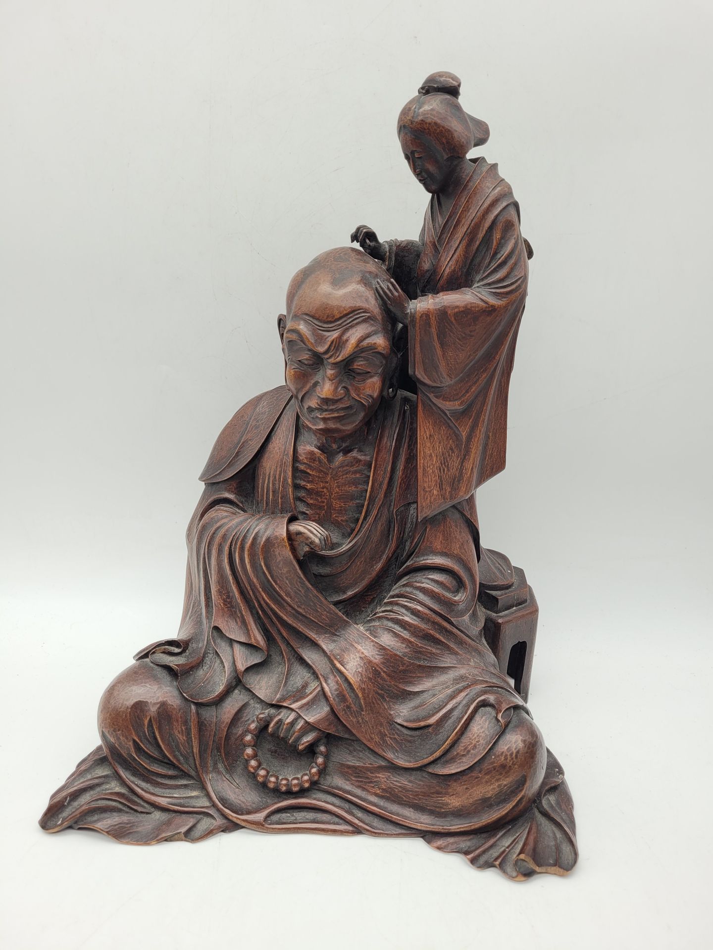 Moine ascète en bois sculpté, Japon, époque Meiji (1868-1912)
Représenté assis, tenant un chapelet bouddhique dans sa main gauche, une servante lui rasant la tête.
Hauteur : 36 cm
Petits accidents.