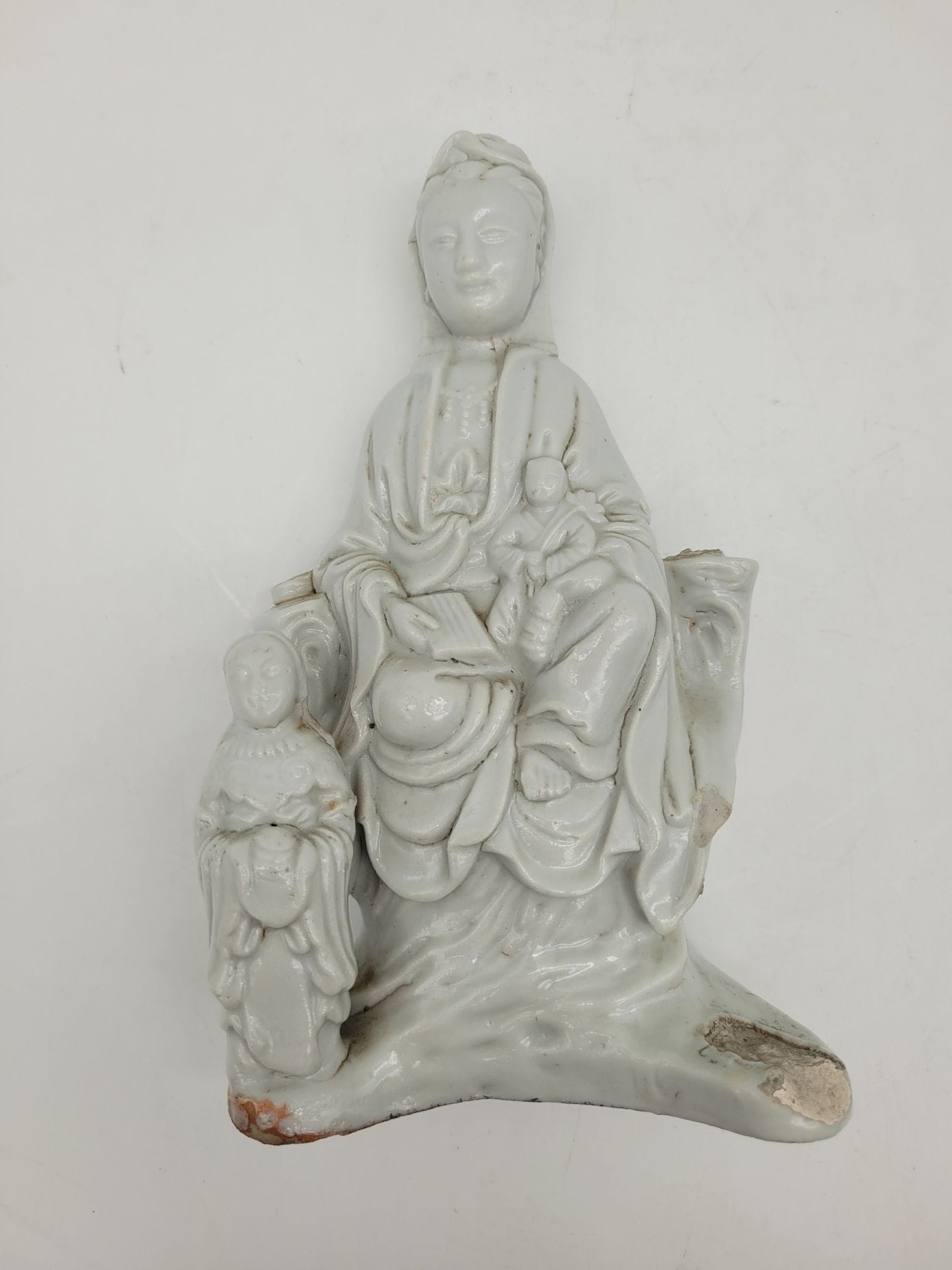 Chinese white porcelain Guanyin, China, 18th century
Seated, right leg bent, left leg dangling in a position known as vamardhaparyaka, and holding a seated child.
Damage and missing parts. The attributes and an acolyte are missing.
Height: 20.1 cm