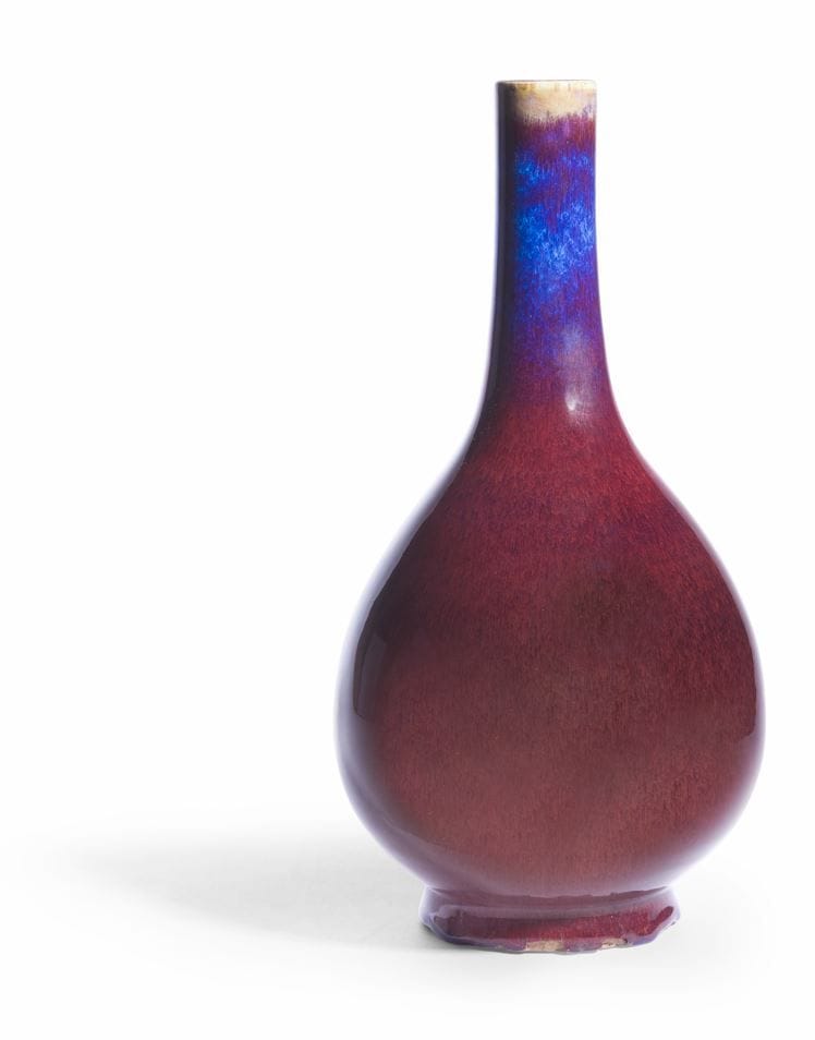 Bottle vase with long tubular neck in porcelain with red flamed glaze, China, 19th century
Resting on a short foot, the slightly cracked glaze is a beautiful deep red, the top of the neck shows celadon ochre-green tones and the neck a beautiful lavender-blue color also present around the foot. The cover has been lightly lapped around the heel. Apocryphal Qianlong six-character mark in underglaze blue on the base.
Height: 39 cm