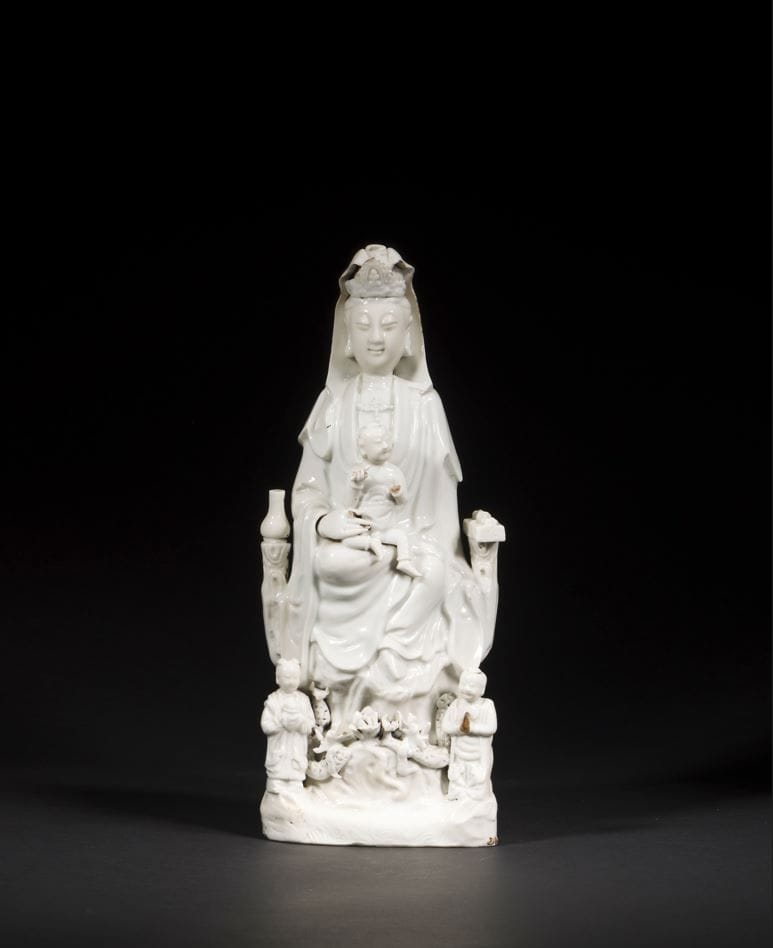 Large Chinese white porcelain Guanyin, China, Dehua, 18th century
Seated with her right leg bent and her left leg dangling in a position known as vamardhaparya?ka, holding a seated child. On one side of her throne, a lustral water bottle on her right, a scroll and sutra books on her left. At his feet, his two acolytes LongNü, holding the Pearl of Light, and ShanCai TonZi, hands in adoration. Between them, on a terrace, a lotus flower surrounded by two facing dragons.
Height: 37 cm
Minor accidents.
