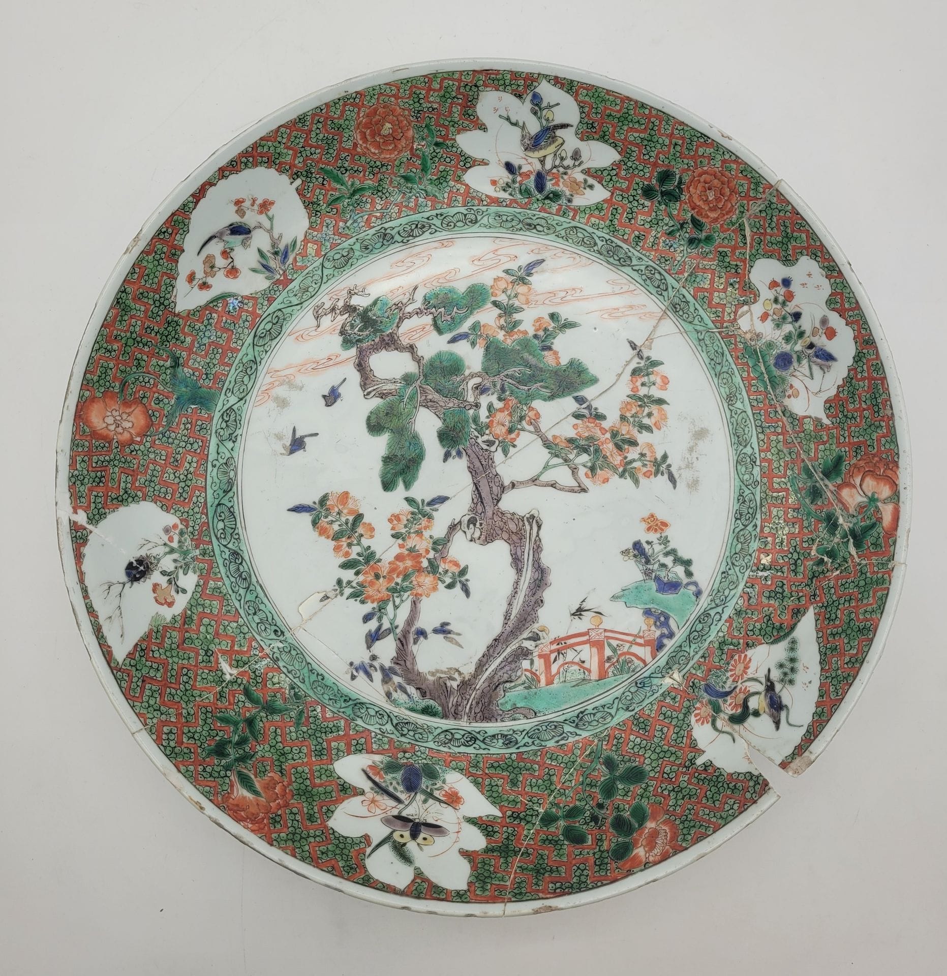 Important plat en porcelaine à décor dit de la famille verte, Chine, époque Kangxi (1661-1722)
A décor central d'arbre fleuri, le marli décoré de réserves en forme de feuilles garnies d'insectes ou d'oiseaux, sur un fond de croisillons rouges et verts.
Diamètre : 38,5 cm
Marque à la feuille.
Cassé en plusieurs morceaux et recollé, ancienne restauration aux agrafes, petits manques.