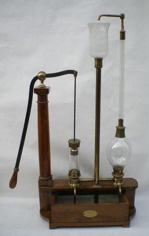 Pompe aspirante et foulante, Breton Frères, à Paris. Très beau modèle, dans l'esprit de celui de l'Abbé Nollet. Corps en laiton verni, cylindre et réserve en verre, socle et colonne en noyer, c. 1835. Rare. (Haut.: 98 cm, Long.: 49 cm)