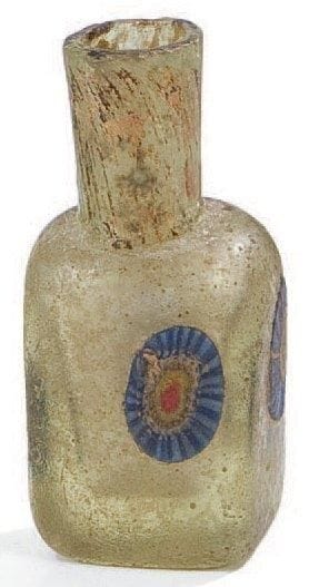Petit flacon en verre, Iran, XIIe-XIIIe siècle Verre moulé à col cylindrique et panse parallélépipédique incrustée sur chaque face d'un «oeil de boeuf» à coeur rouge et cerne radiant bleu. Trace de dorure sur le col. H.: 6 cm (Usures)  Sur ce type de flacon, voir S. Carboni et D. Whitehouse, Glass of the Sultans, Londres, 2007, p. 86-87