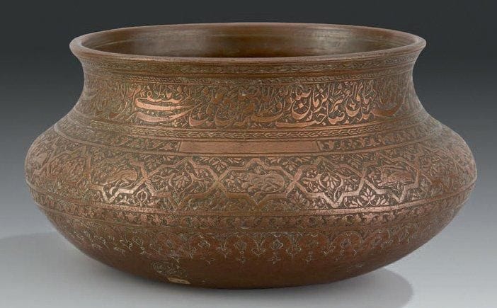 Bassin tâs en cuivre, Inde, XVIIe-XVIIIe siècle Cuivre ciselé, à fond plat, panse bombée et ouverture cintrée. Décor sur la paroi extérieure d'un bandeau épigraphié en nasta'liq sur fond fleuri en partie haute, invoquant les noms de Muhammad et des 12 imams. Sur la moitié inférieure, frise de cartouches étoilés meublés d'animaux alternés de compositions de palmes, sur fond fleuri, et bordé d'une frise fleuronnée. Deux petites marques de propriétaires dans des médaillons sous la base. D. ouverture: 20 cm - H. 13 cm (Fond réparé)