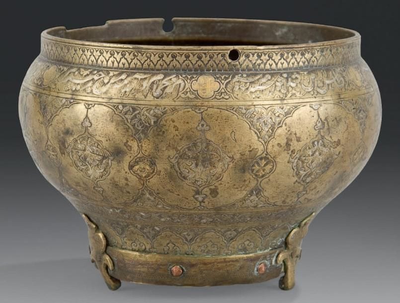 Seau de bain, satil, aux mandorles, Iran de l'Ouest, XVIe siècle Laiton ciselé, incrusté d'or et d'argent. Panse cintrée, ceinturée d'un large bandeau meublé de médaillons polylobés aux mandorles festonnées ornées de rinceaux de demi-palmettes, et écoinçons fleuris. Frise poétique inscrite dans des cartouches en nasta'liq sous le bord, interrompus de médaillons quadrilobés portant une dédicace au propriétaire. A la base, frise de trilobes surmontant des pendentifs fleuronnés garnis de rinceaux. D.: 18,3 cm - H.: 14 cm (Accident, fond rapporté, manque l'anse) Ce seau de bain, bien qu'accidenté, est tout fait remarquable, par la qualité de son décor et sa forme. Il peut être rapproché d'un seau conservé au Victoria and Albert Museum sous le numéro d'inventaire 222-1892, et publié dans A.S. Melikian Chirvani, Islamic Metalwork from the Iranian World 8-18th centuries, Londres, 1982, cat.135