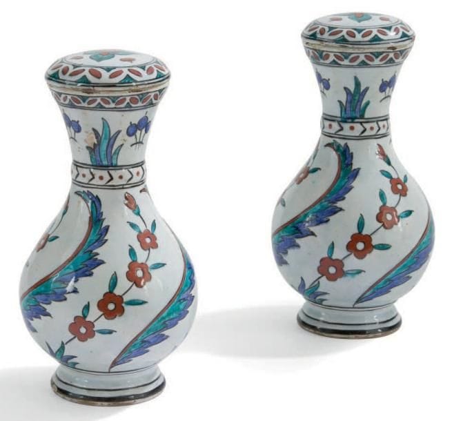 Paire de petits vases couverts de style Iznik, France, fin du XIXe siècle Céramique à panse ovoïde, petite base annulaire et col évasé. Décor peint en polychromie sur fond blanc, de feuilles sâz alternées de tiges d'églantines ondulées sur la panse, et bouquets alternés de touffes de feuilles sur le col. Petit couvercle bombé orné d'un large trilobe. Ancienne étiquette sous le couvercle "Au vase étrusque. Paris, 20 bd Malesherbes". H.: 24 cm (Eclats sur les couvercles et à la base)