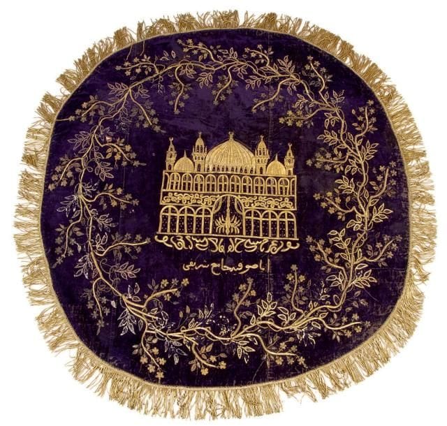 Intéressante tenture ronde brodée de la mosquée Aya Sophia, Turquie, début du XIXe siècle Velours violet en trois parties, brodé de fils métalliques dorés en kabarma et agrémenté de perles, pastilles, et franges. Décor d'une mosquée à coupoles et quatre minarets sur fond de rinceaux fleuris, agrémentée d'une inscription donnant: «Aya Sophia la noble grande-mosquée». Doublure de coton beige. D.: 110 cm (Usures, quelques trous et manques dans les broderies) Cette tenture ronde était probablement utilisée comme couverture de table à café cérémonielle. Nous n'en connaissons que peu d'exemples qui peuvent lui être comparés, comme celle vendue par Sotheby's Londres, 23 avril 2012, lot 642, ou encore celle conservée au Sadberk Hanim Museum, inv. 3038-l.417, et publiée dans N. Atasoy, Splendors of the Ottoman Sultans, 1992, p. 259. Dans ces deux cas, la mosquée représentée n'est pas identifiée. En effet, rares sont les textiles ottomans figurant un édifice précisément identifié par une inscription, comme c'est le cas ici. Pour deux autres exemples, utilisant ce même motif de la mosquée Aya Sophia voir les catalogues de Sotheby's Londres, le 5 octobre 2011, lot 354, et Christie's South Kensington, le 13 octobre 2006, n° 166