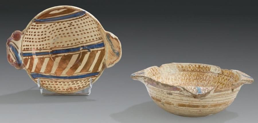 Deux bols à oreilles, escudillas, Manises XVIe-XVIIe siècle Faïences hémisphériques à deux et quatre oreilles polylobées. Décor de lustre métallique et rehauts cobalt. Sur l'un, large bandeau hachuré sur fond meublé de petits tirets, et sur l'autre, blason sur fond de «solfa». Décor de cercles concentriques et spirales à l'extérieur. D.: 14 cm et 14,5 cm (Manque une oreille restaurée, éclats au rebord)
